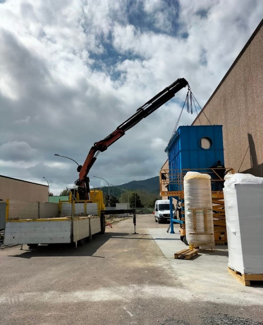 Cantiere edile con gru che scarica materiali accanto a un edificio beige sotto un cielo nuvoloso.