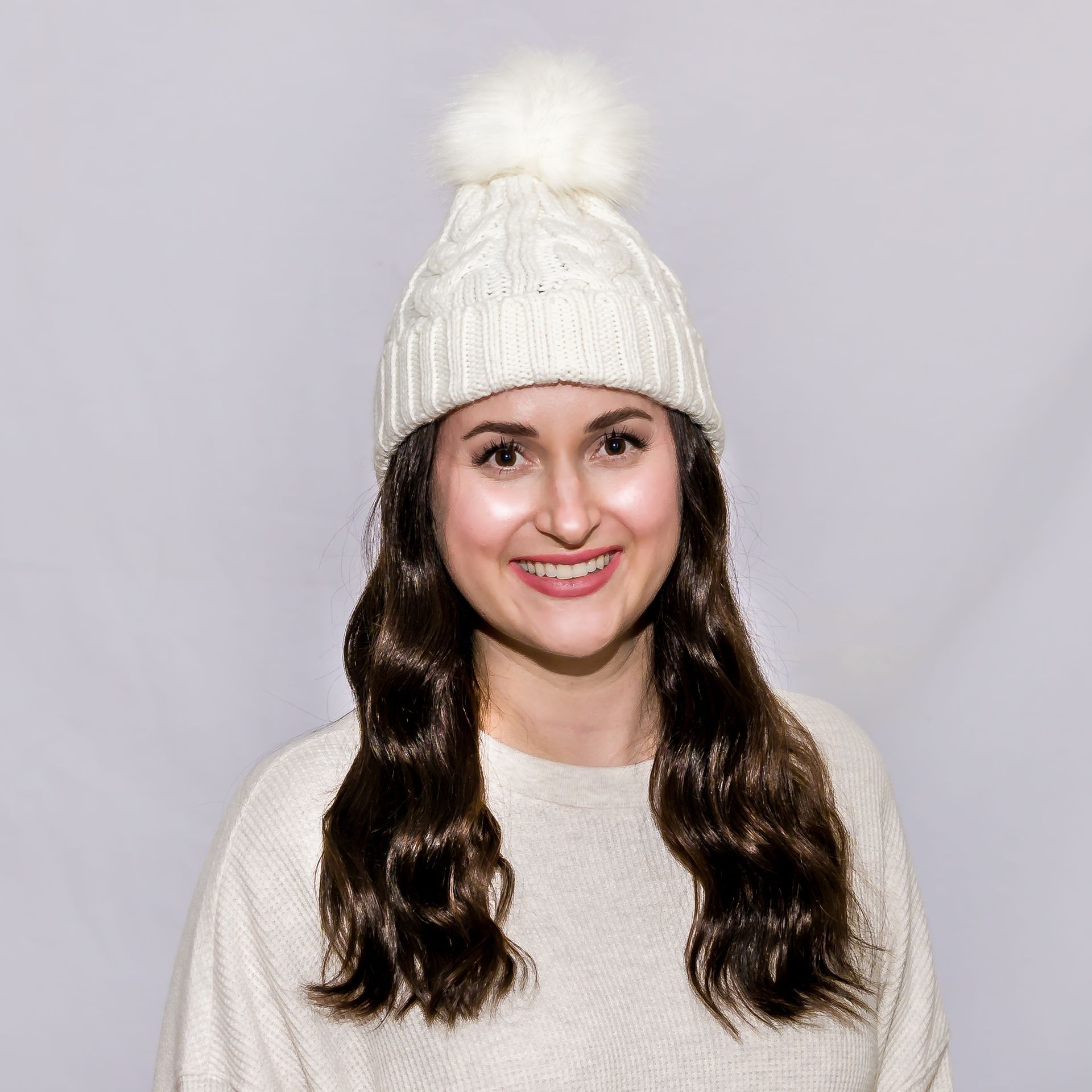 Woman in a cream-colored cable knit hat and sweater, smiling.