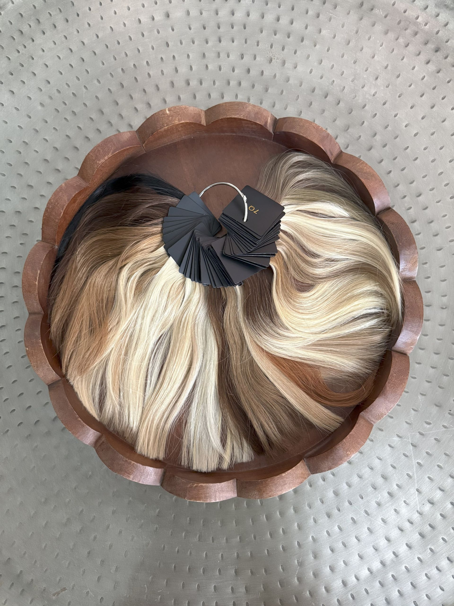 Wig with blonde, brown, and black hair in a circular, scalloped wooden frame.