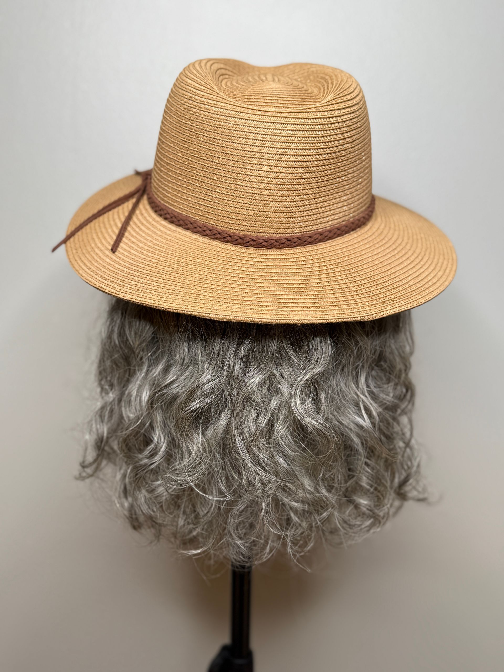 Tan straw hat with brown band, resting on a gray wig.