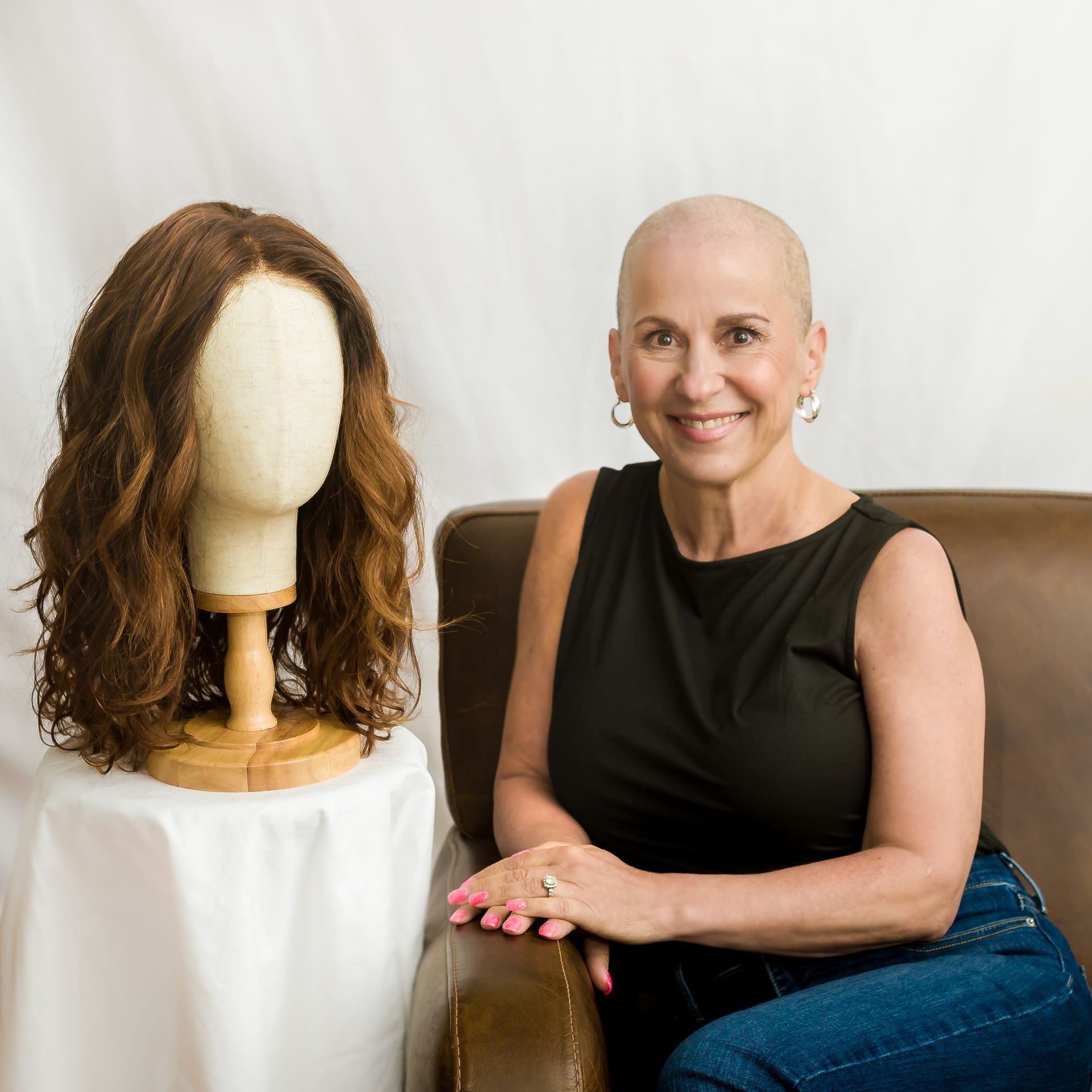 A person's hands sewing hair onto a wig cap. Three mannequin heads with wigs are in the background.