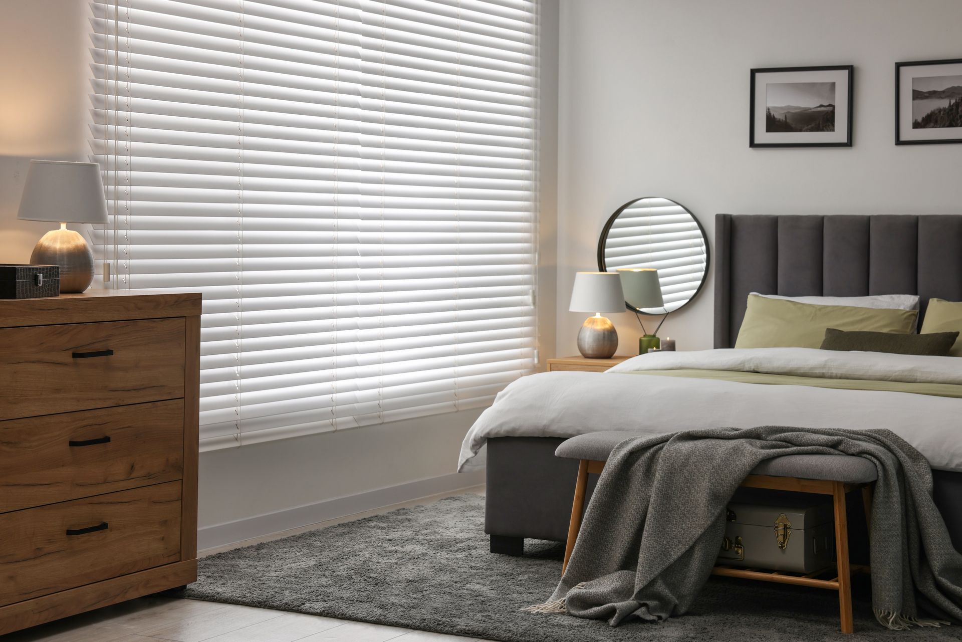 A bedroom with a bed , dresser , mirror and blinds.