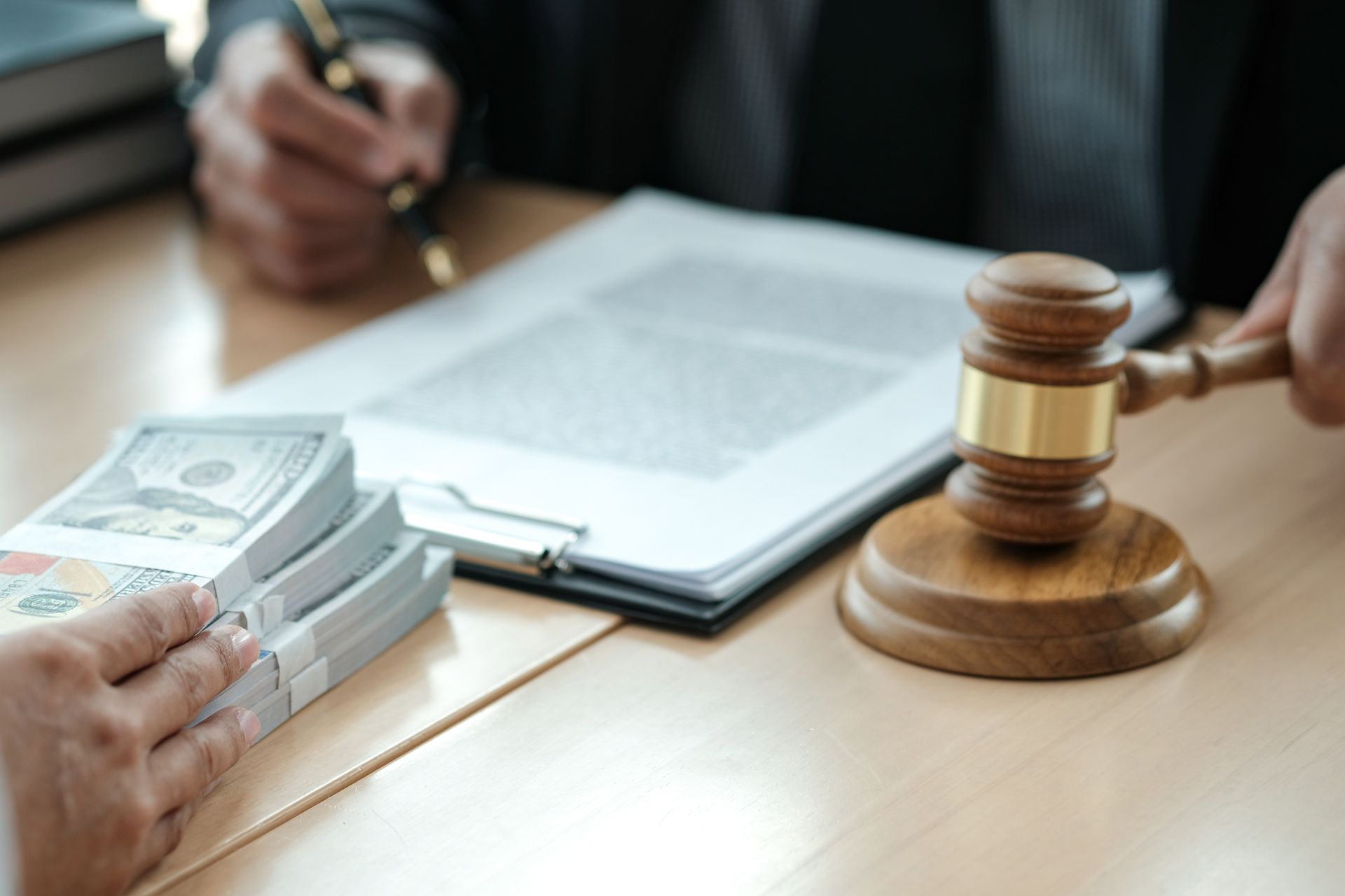 Person handing cash near a judge's gavel and legal documents.