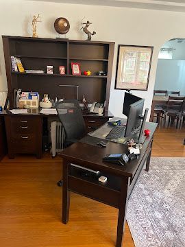 A home office with a dark wood desk, hutch, black mesh chair, dual computer monitors, and decorative figurines.