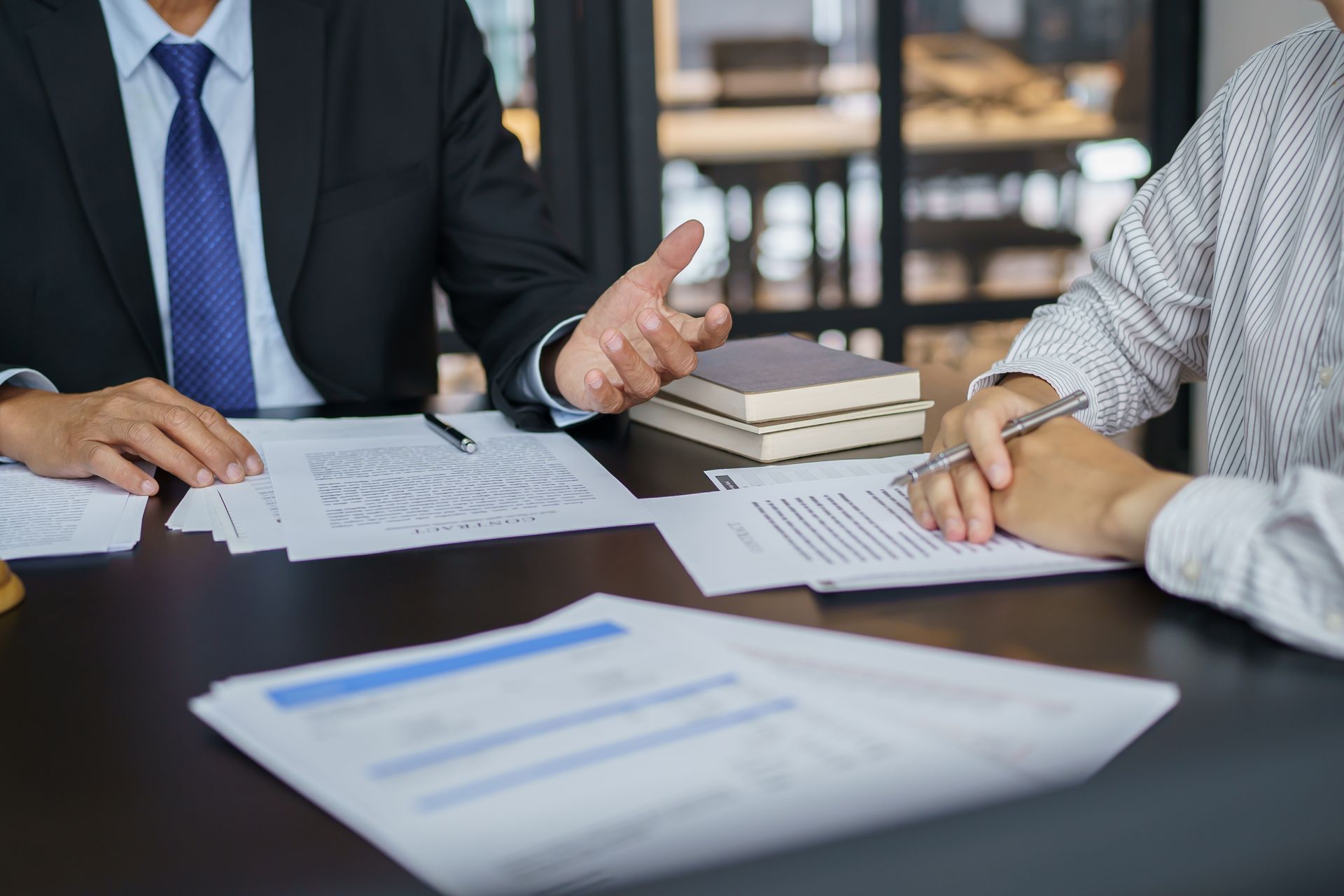 Two people sit at a desk reviewing documents and discussing business in an office setting.