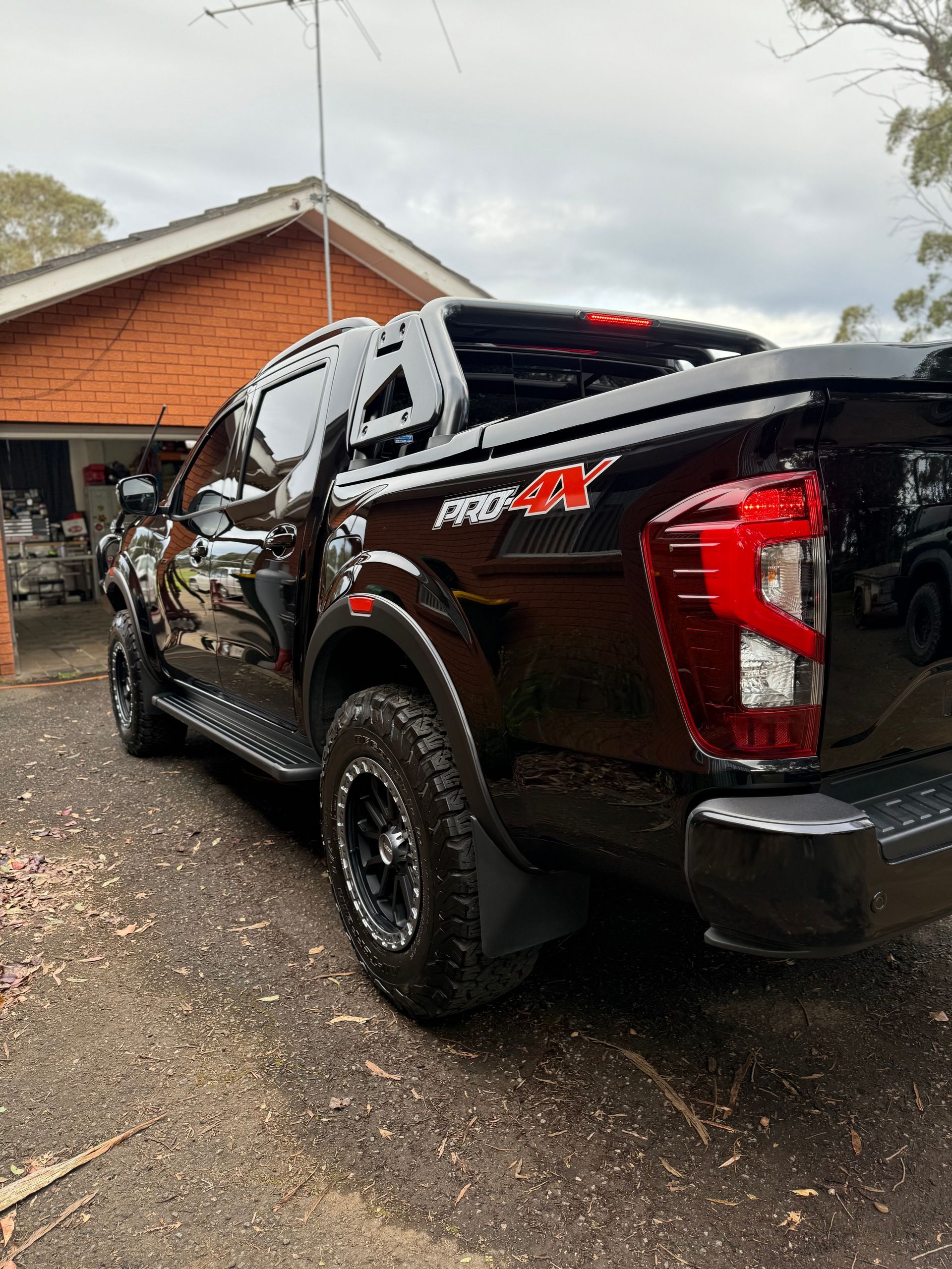Black Nissan Navara Pro-4X pickup truck parked in a driveway with a house in the background.