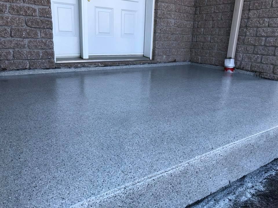 Un porche en béton gris avec une porte blanche en arrière-plan.