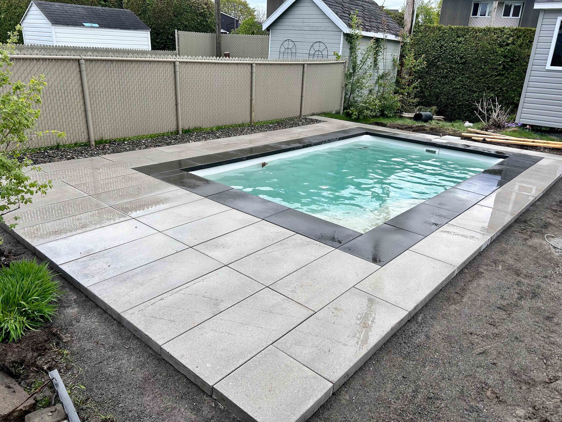 Piscine dans le jardin avec eau bleu clair, terrasse en pierre grise et clôture en bois pour plus d'intimité