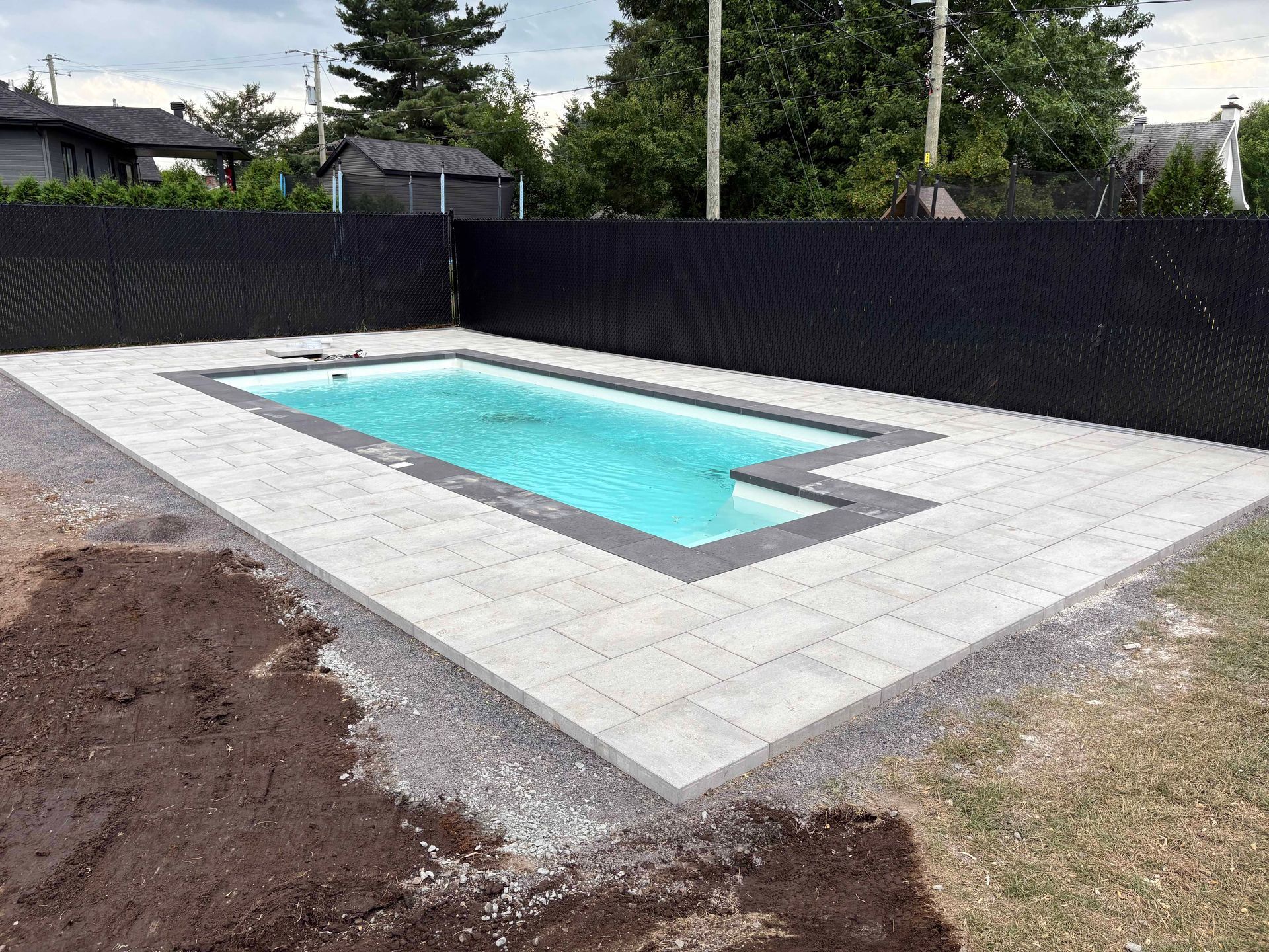 Piscine dans le jardin avec eau turquoise, dallage gris et clôture noire pour plus d'intimité