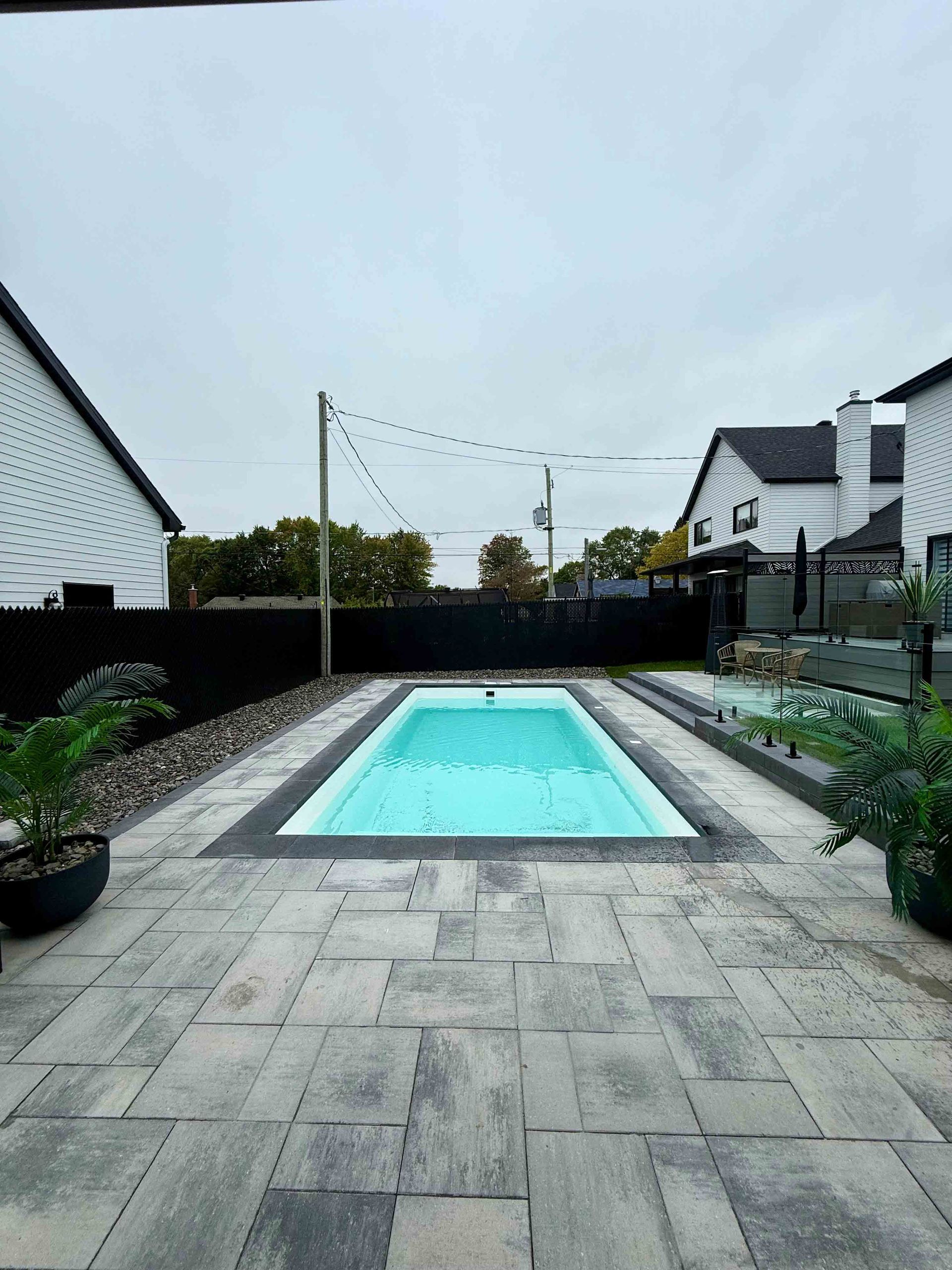 Terrasse arrière avec une petite piscine rectangulaire turquoise, dallage en pierre et maisons de chaque côté.