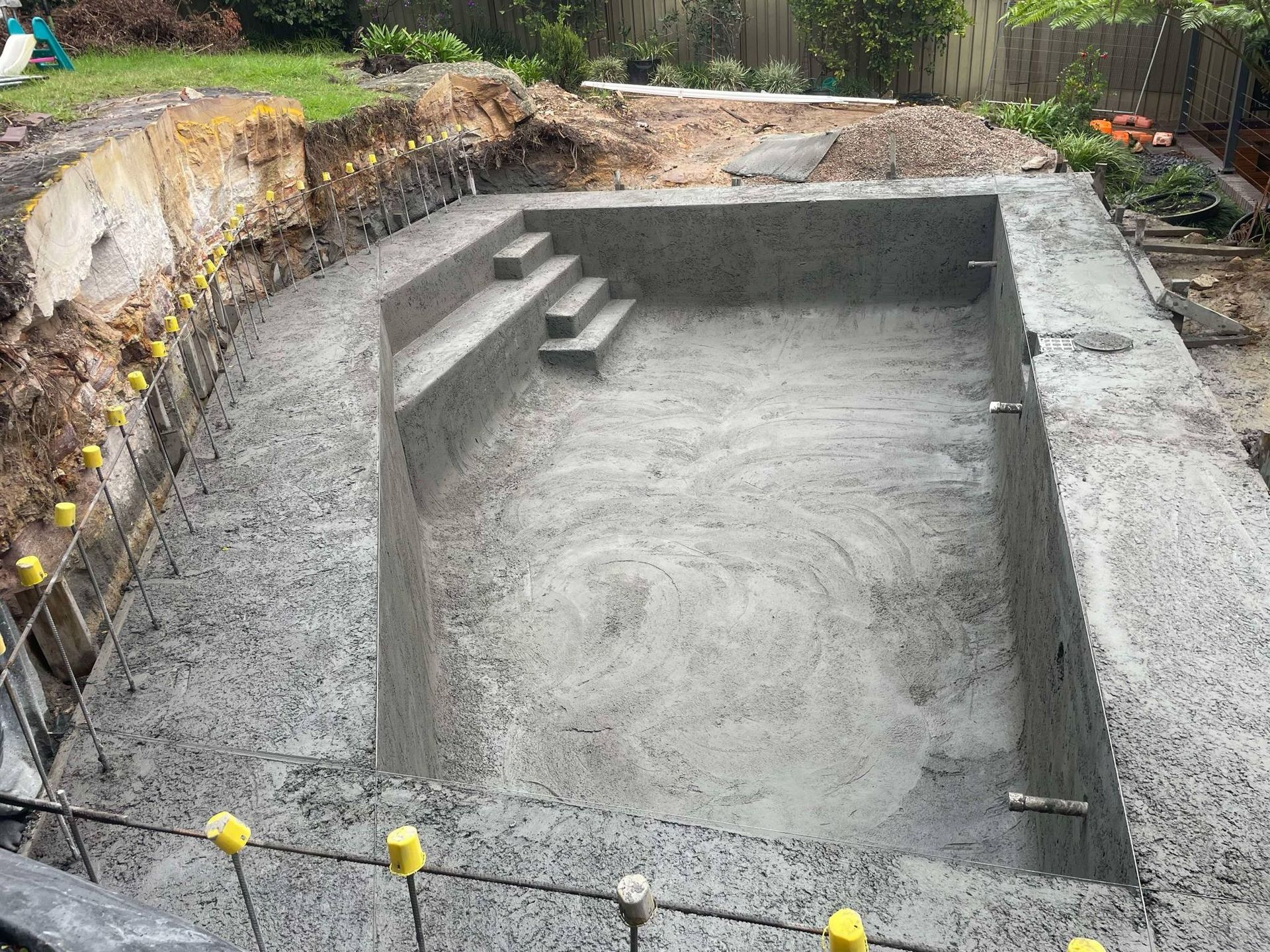 Concrete backyard pool under construction with steps and gray plaster walls
