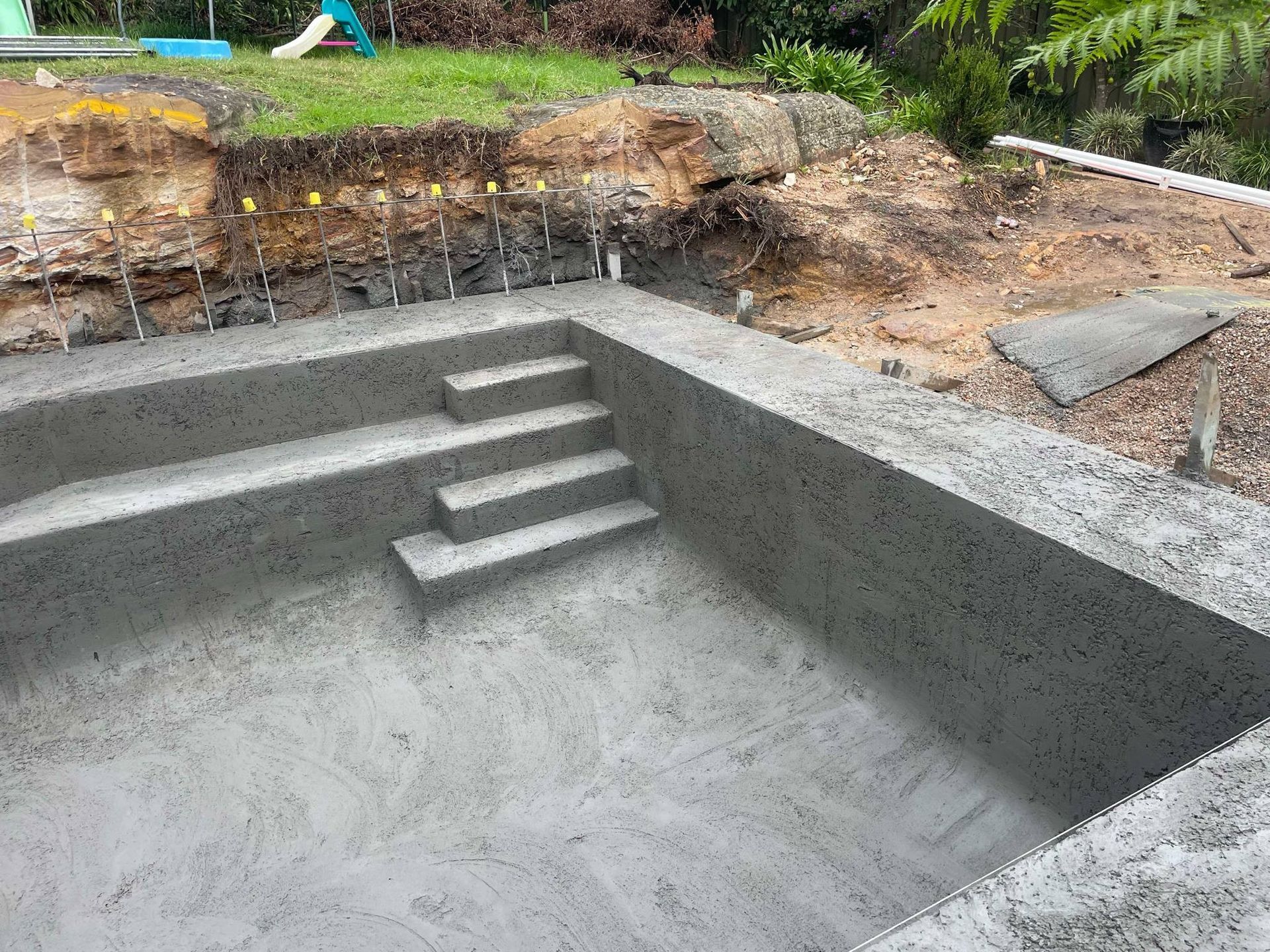 Concrete pool under construction with built-in steps and surrounding dirt hillside