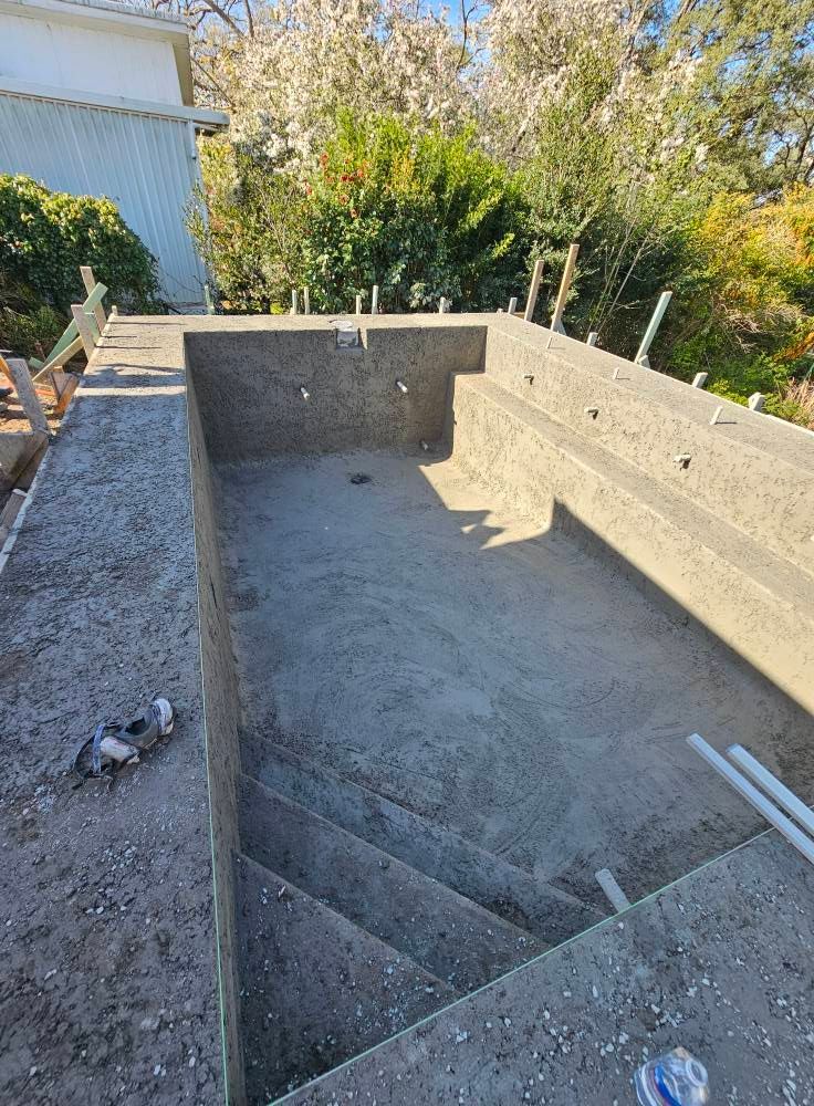 Empty concrete swimming pool under construction with steps and surrounding greenery