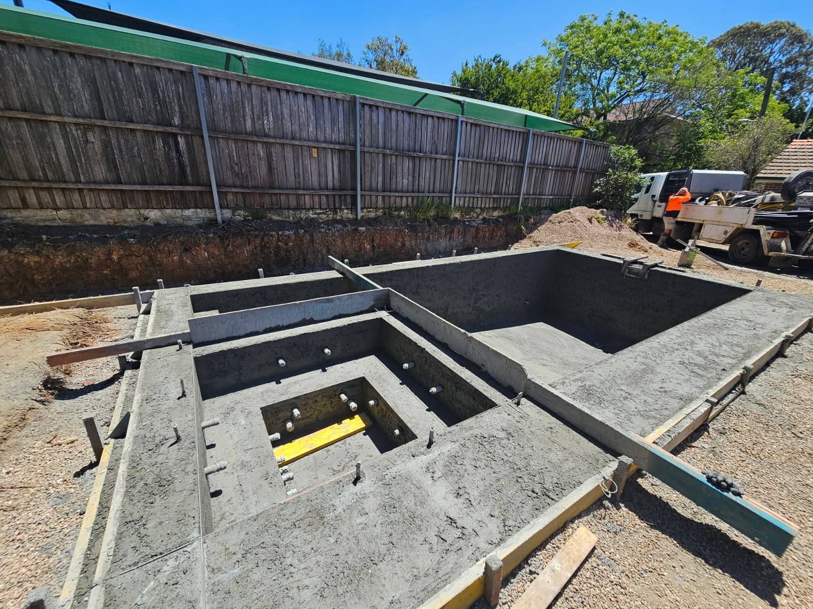Concrete foundation excavation with stepped trenches and workers near construction equipment outdoors