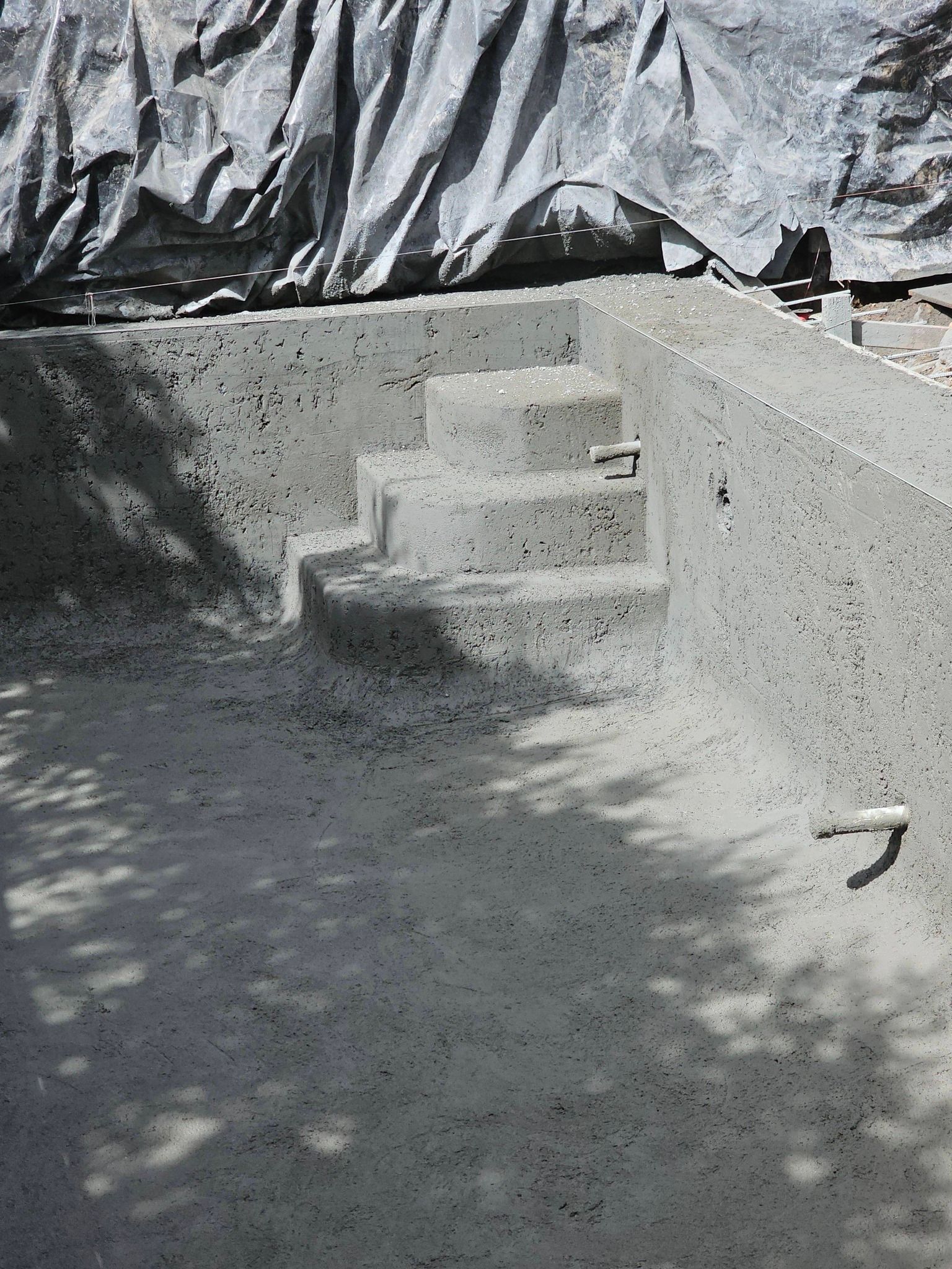 Concrete steps in a small walled outdoor area, with a tarp draped in the background.