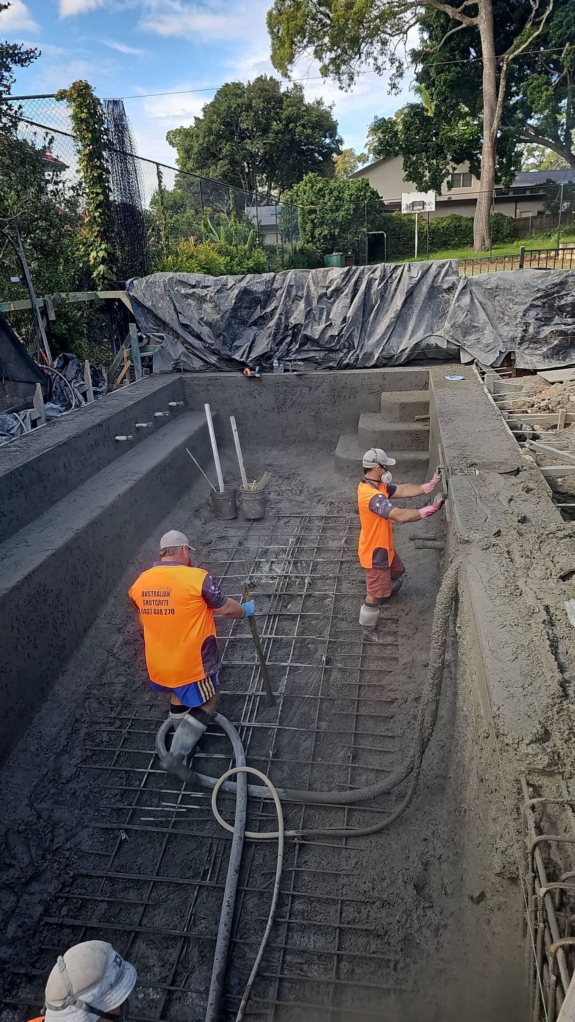 Workers in orange safety gear inside a deep excavation site, with ropes and equipment visible.