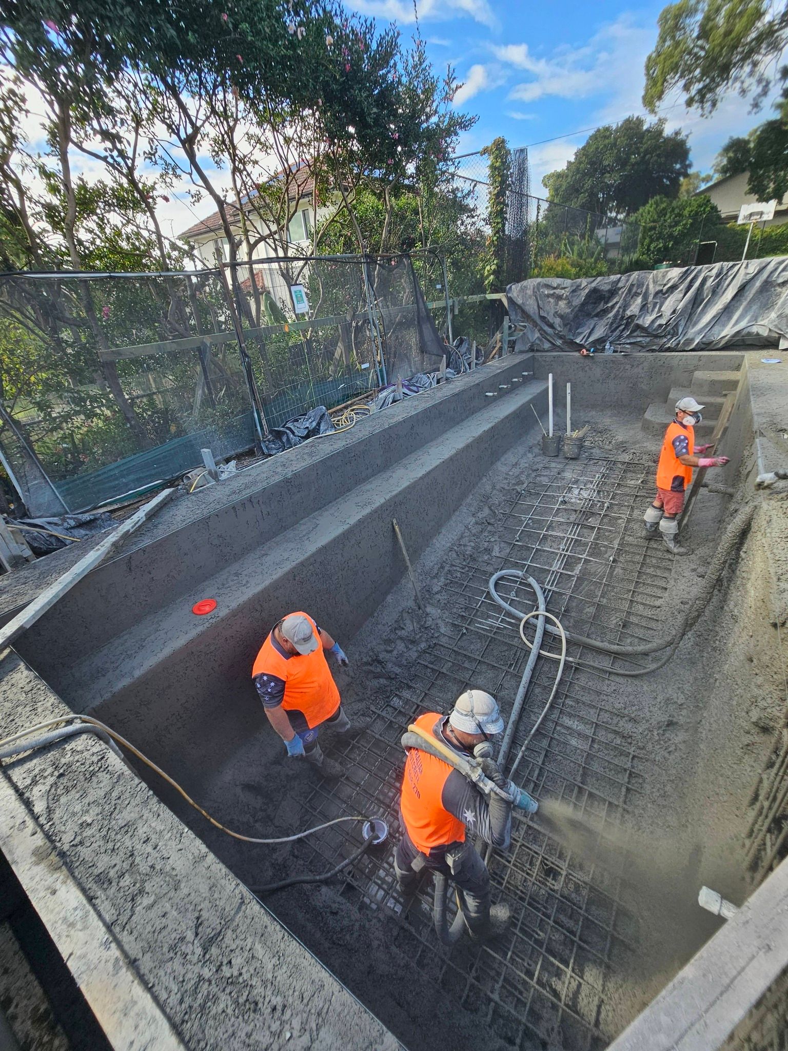 Three workers in orange safety gear dig in a deep trench at an outdoor construction site.