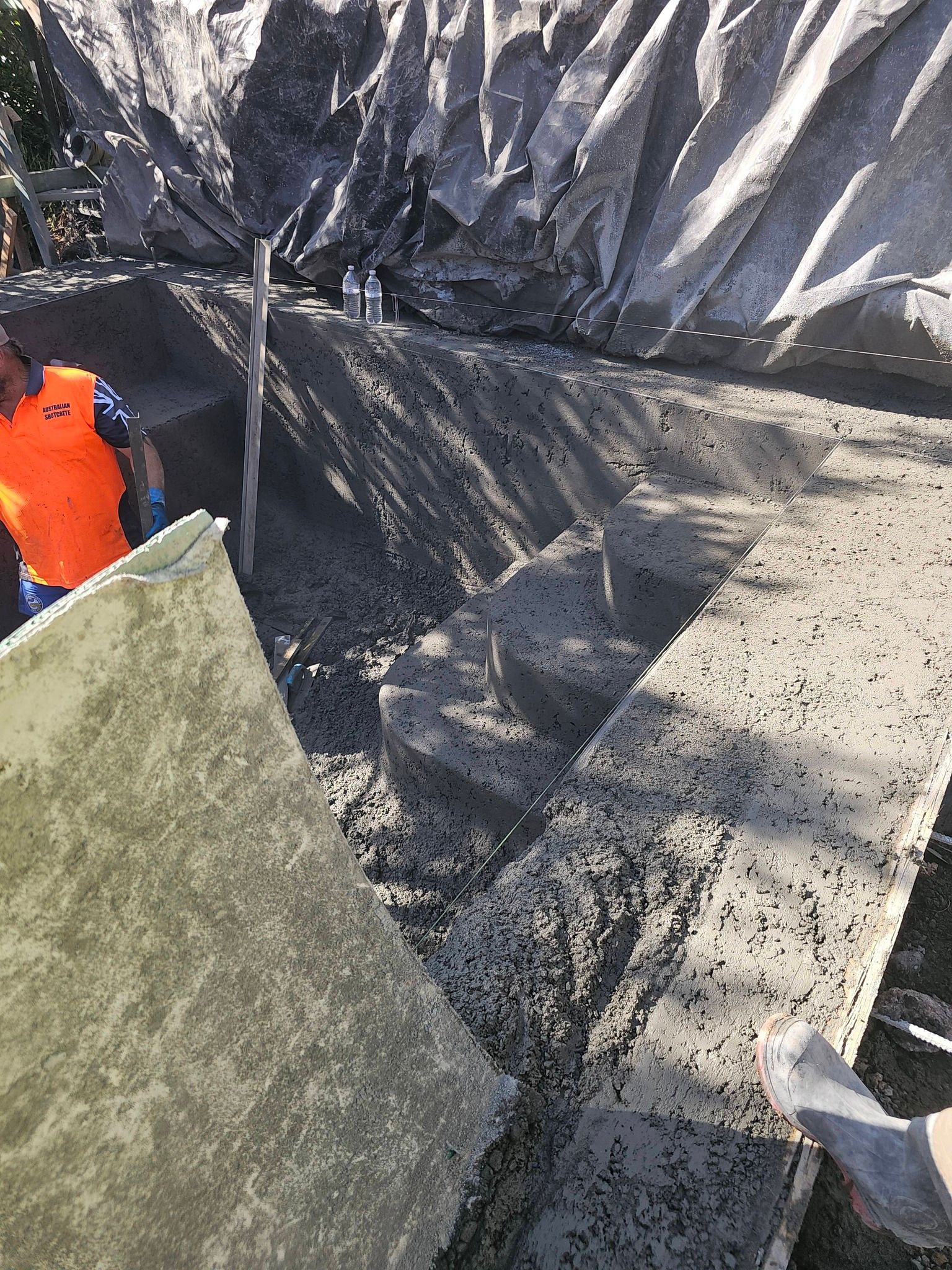 Worker in orange safety vest beside a concrete wall at a construction site.