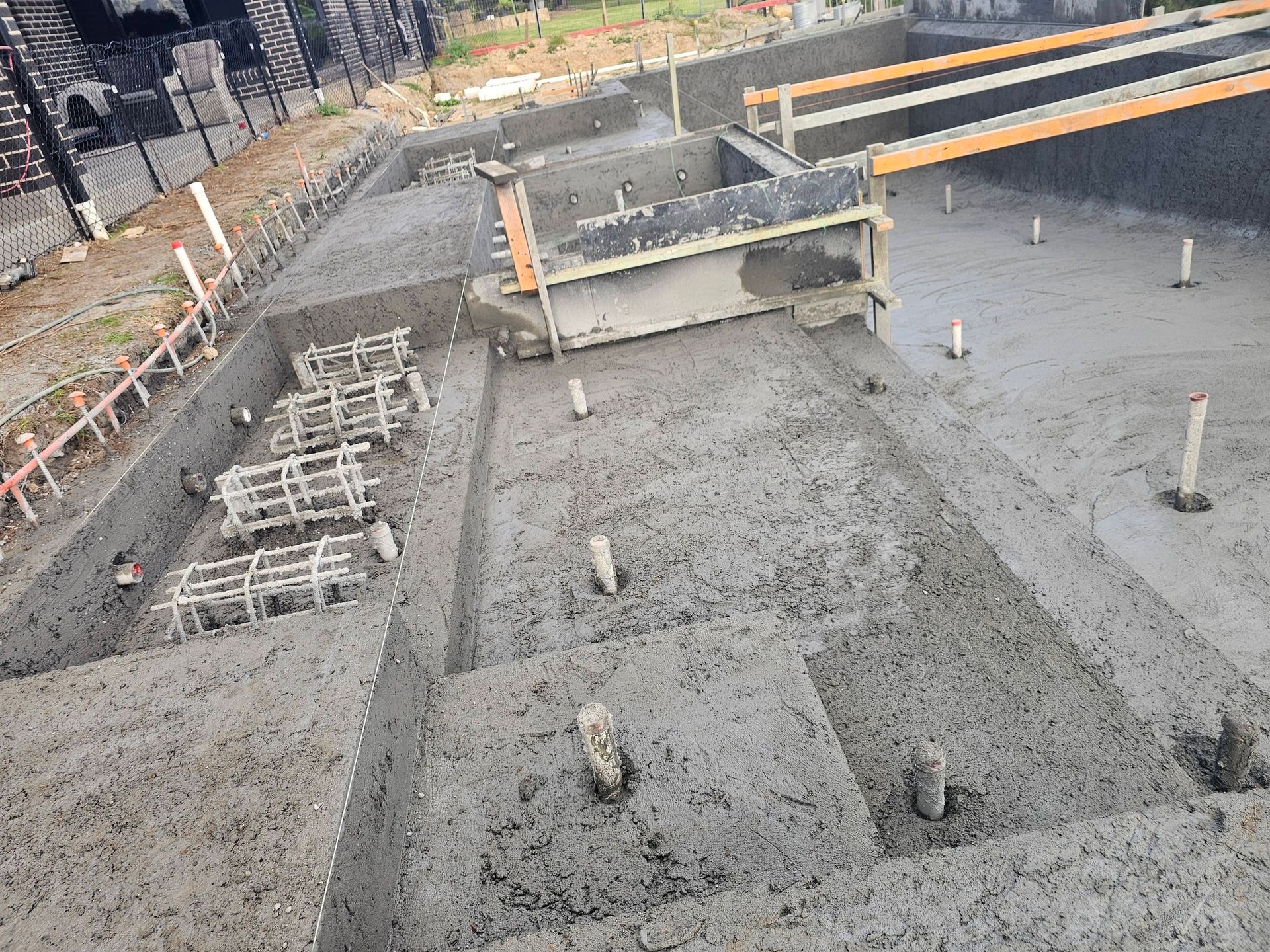 Construction site with concrete foundation slab, rebar cages, and wooden forms under build-up.