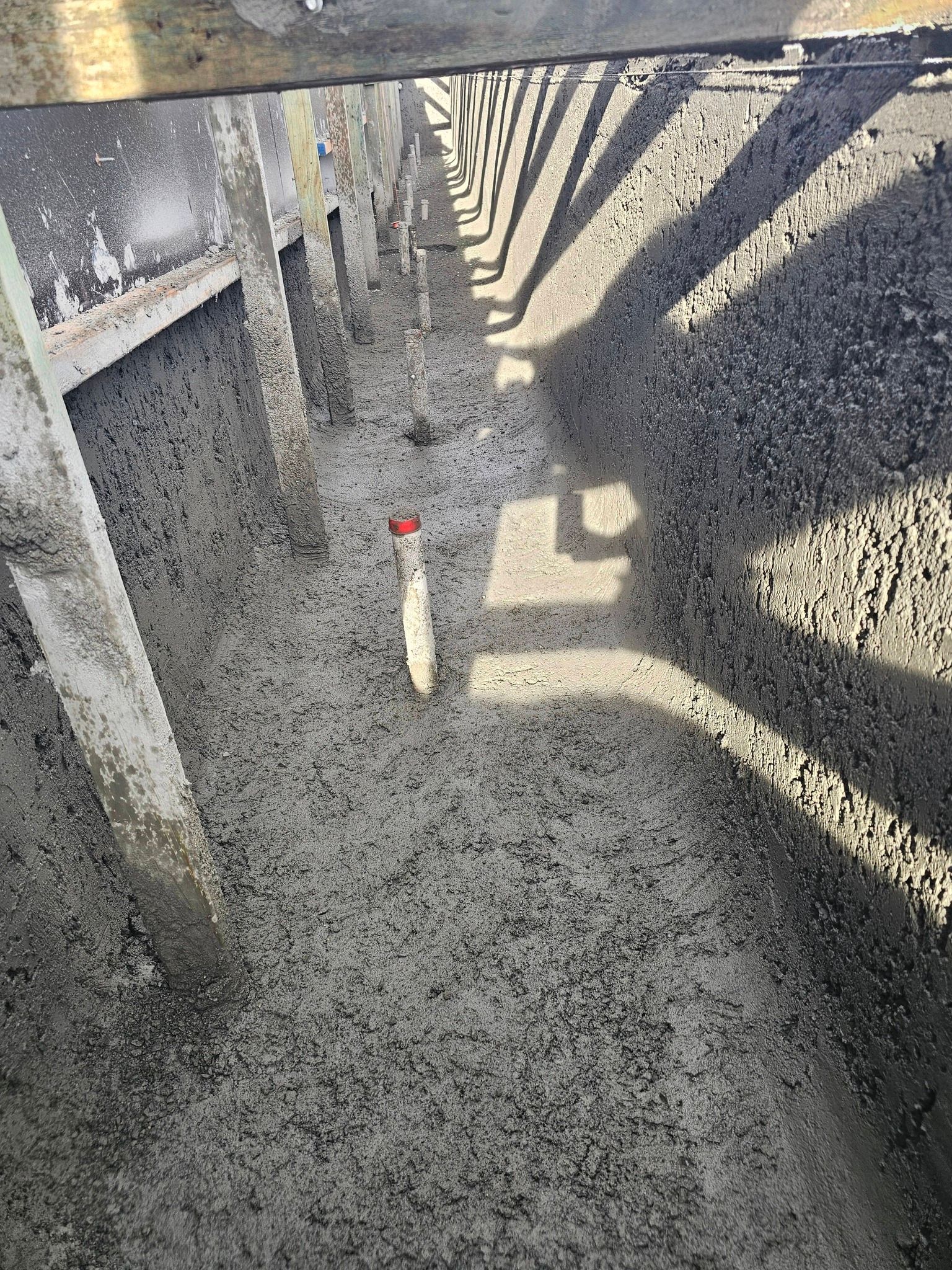 Narrow concrete trench with rough gray walls and a small white stake marker with a red top.