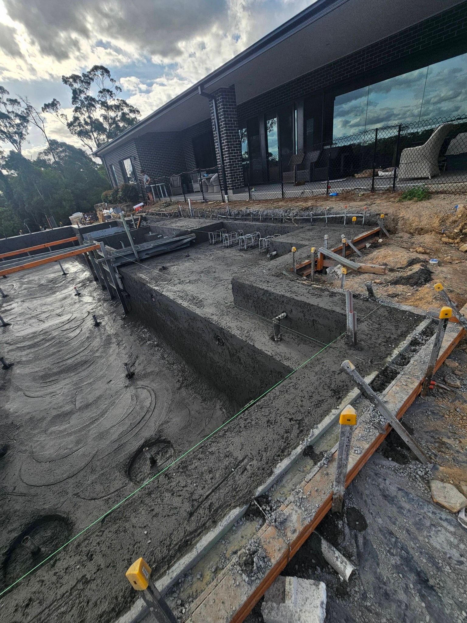 Construction site with a large excavated pit beside a modern glass building and safety barriers