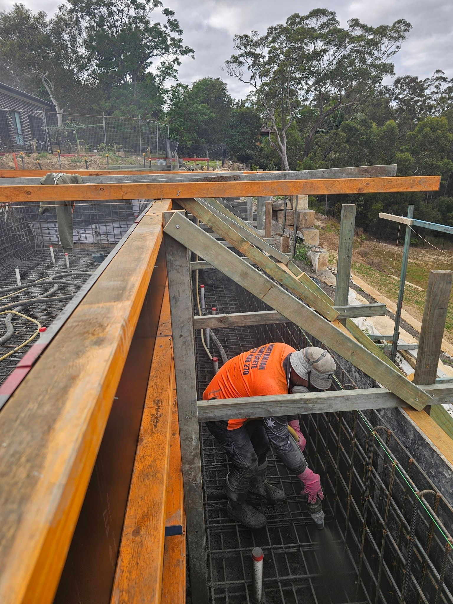 Worker in orange vest and hard hat on a metal roof frame at a construction site.