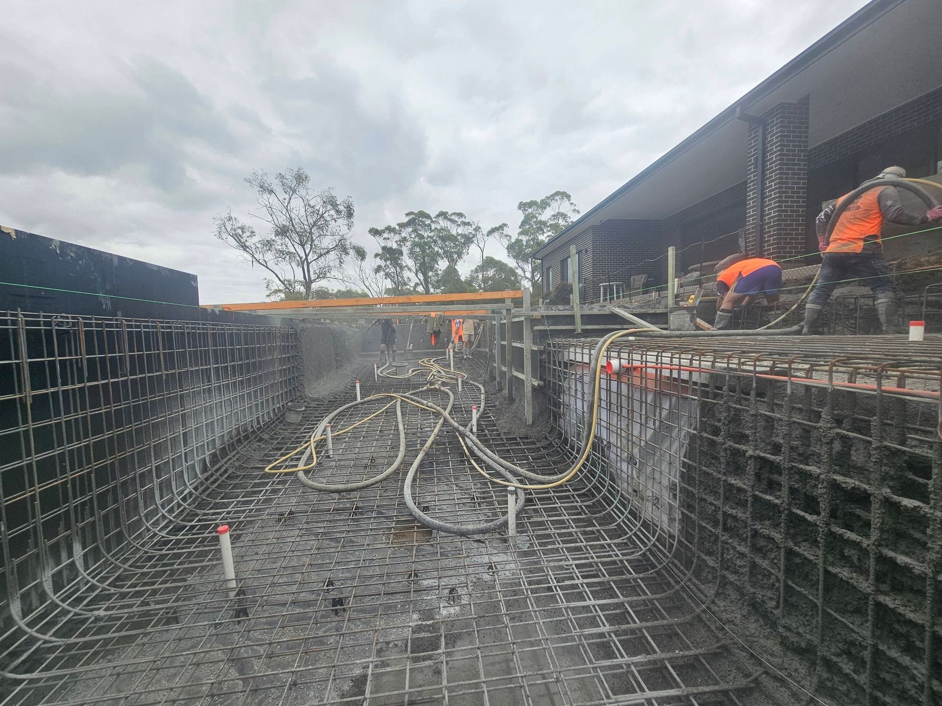 Construction workers on a rebar foundation site, with hoses and an overcast sky.