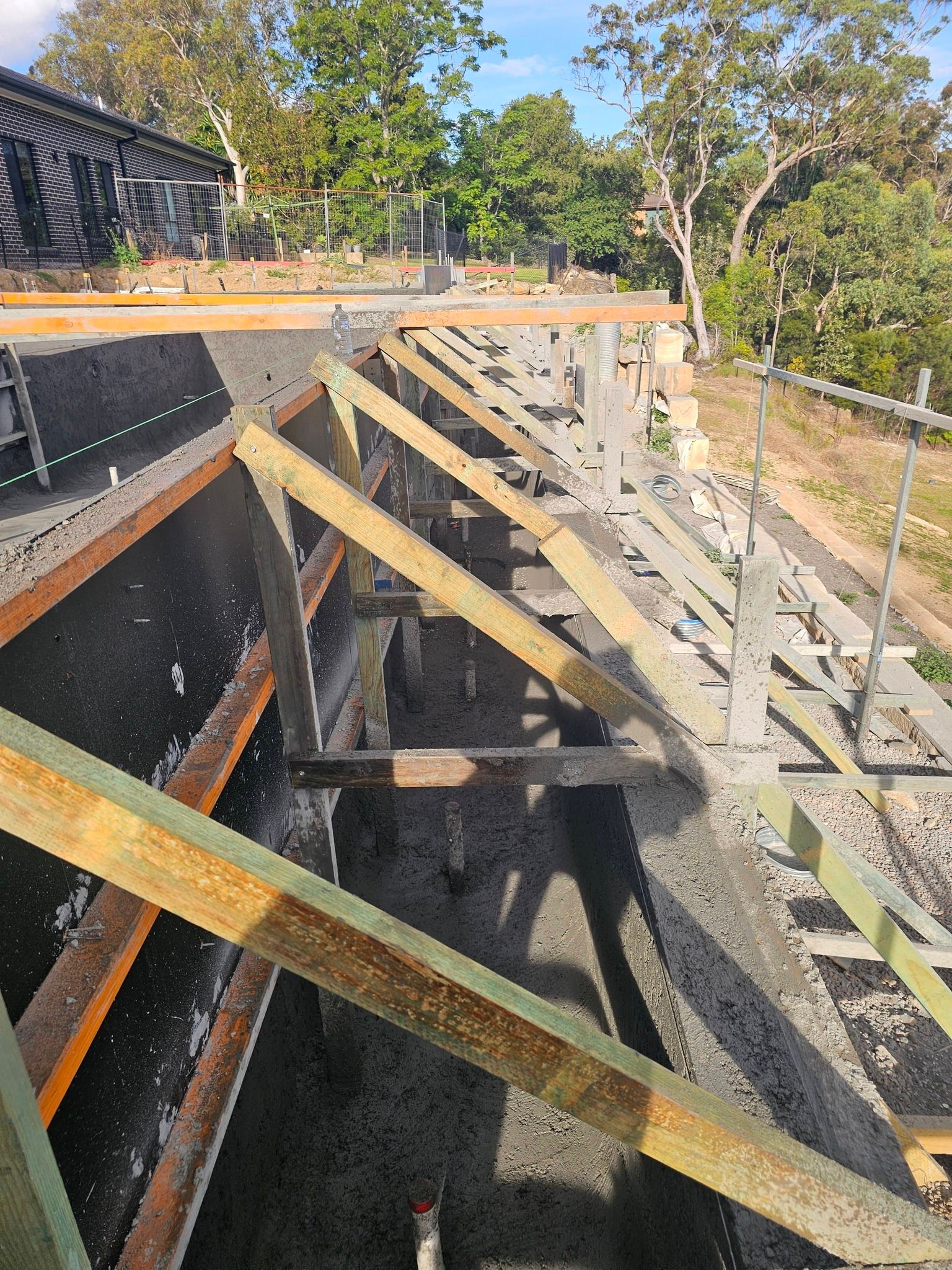 Partially built wooden deck frame with diagonal braces along a sloped hillside under trees