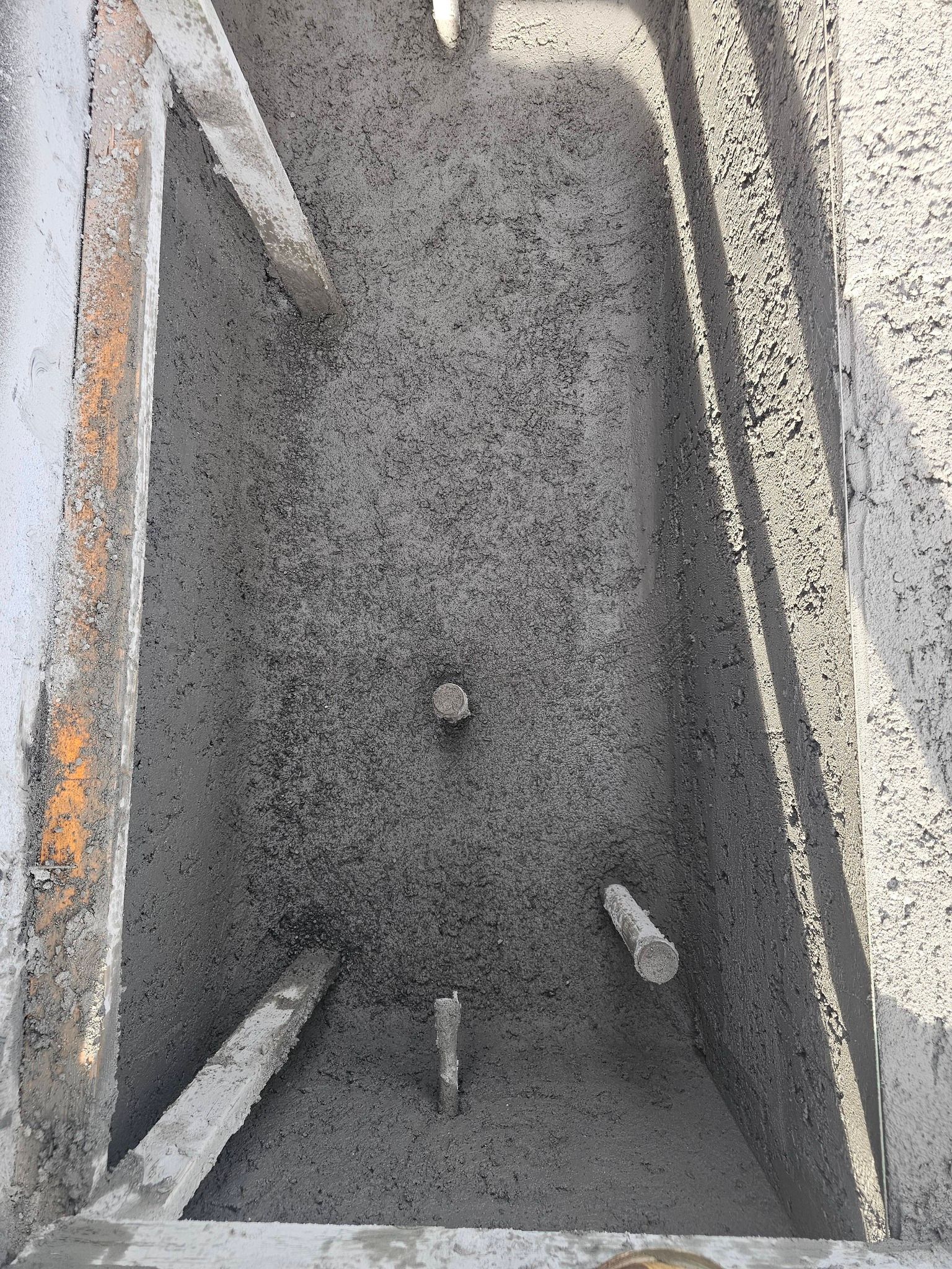 Narrow concrete trench filled with gravel and small debris, viewed from above