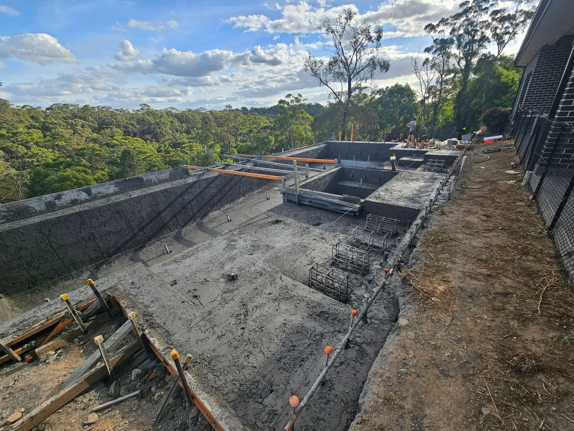 Construction site with fresh concrete foundation, rebar, and formwork overlooking a wooded landscape