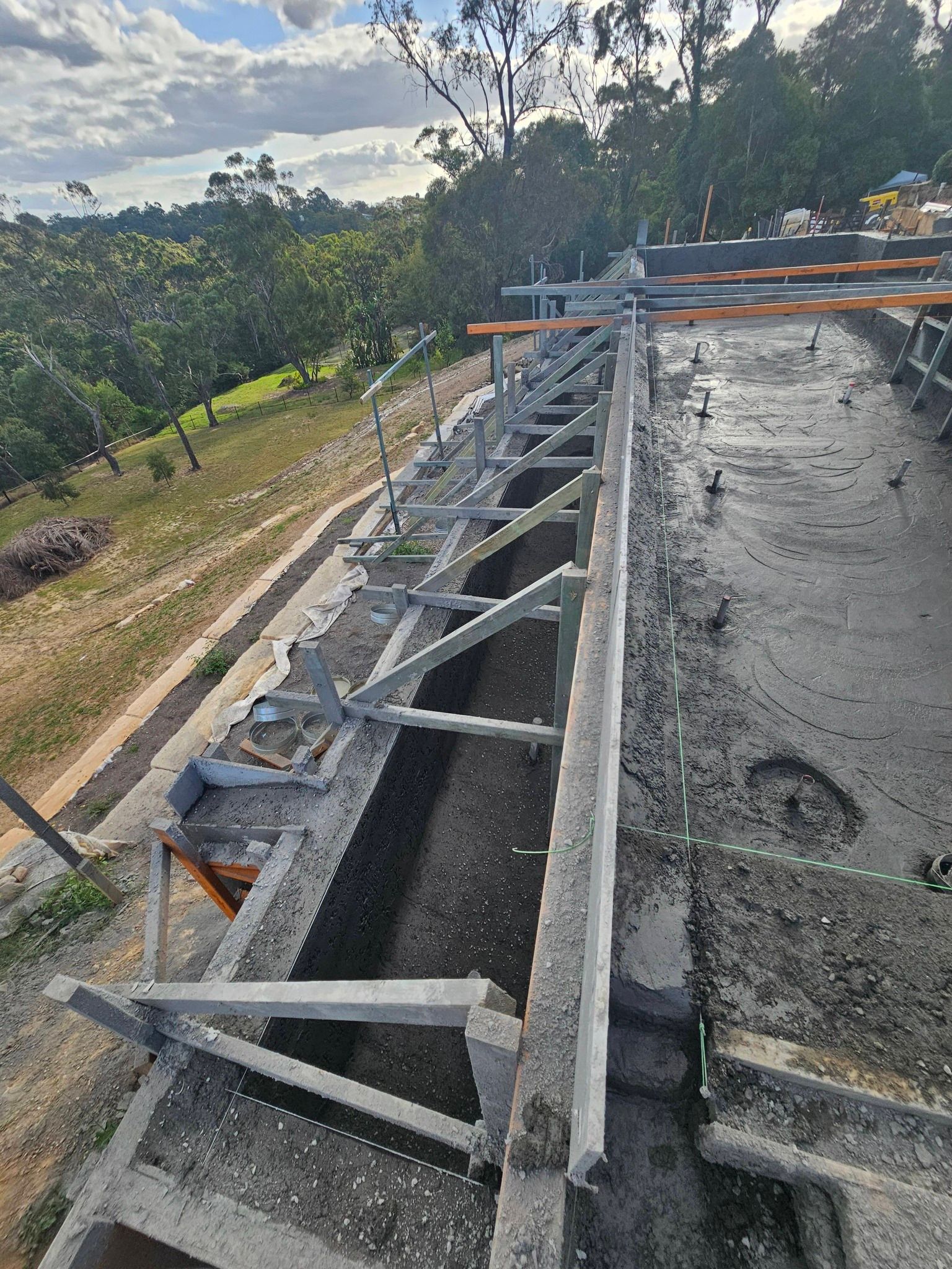 Rooftop construction with steel framing and concrete surface beside trees and a dirt road