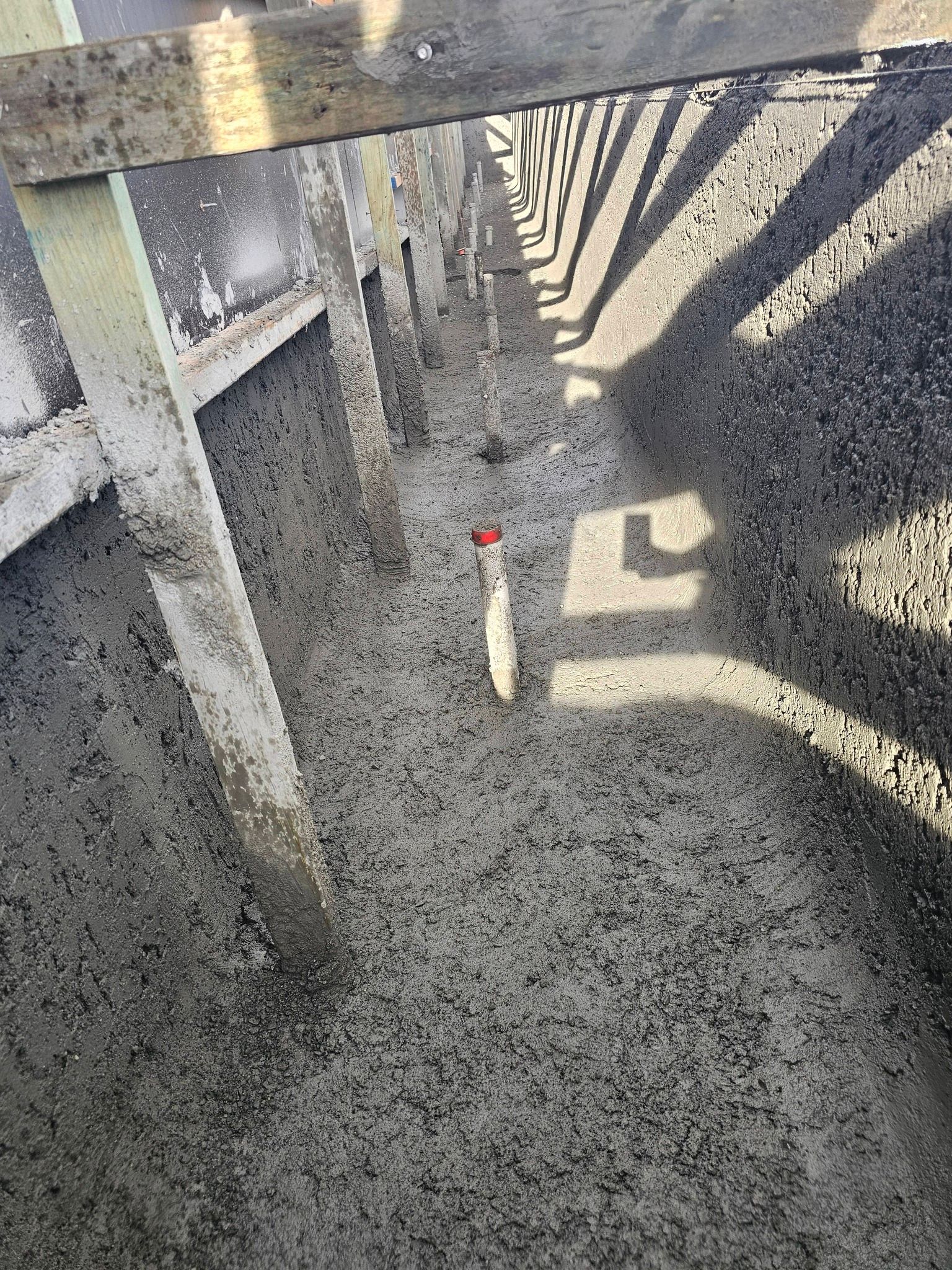 Concrete walkway beside a striped safety barrier, with gravel below and a small marker post in the center.