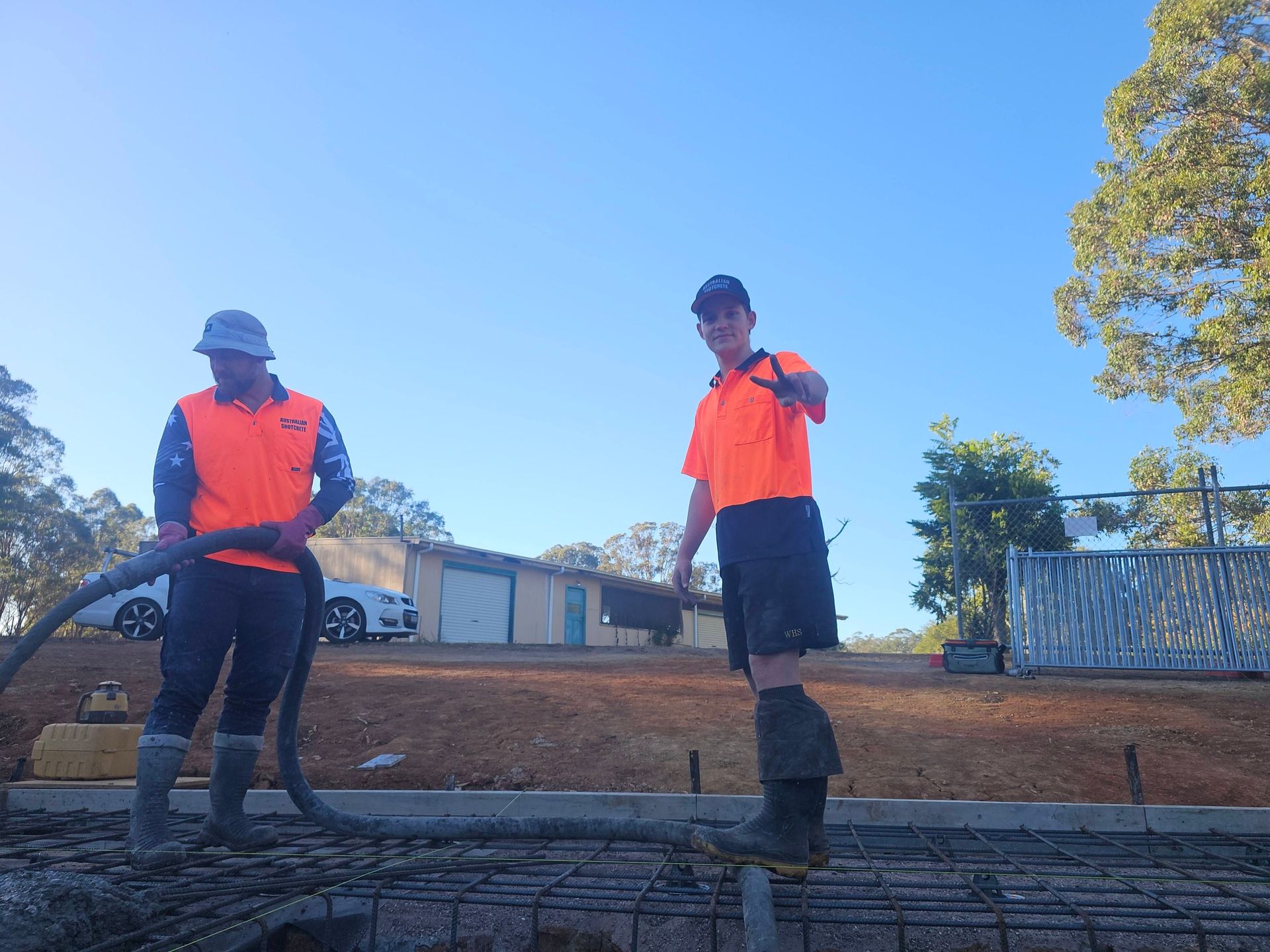 Two workers in orange safety vests stand beside a trench at a construction site