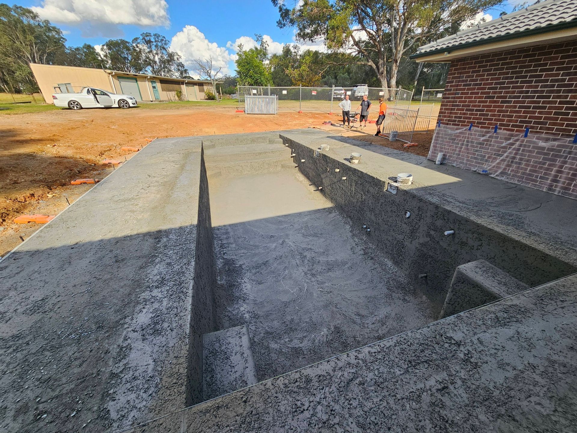Concrete ramp and steps beside a brick building at a construction site, with workers in the background.