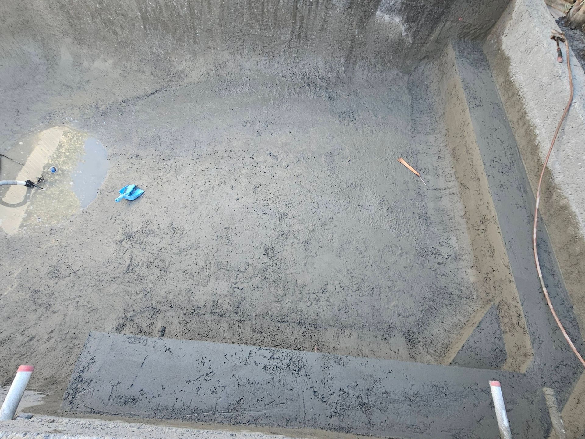 Empty concrete pit with rough gray walls, a small blue object on the floor, and pipes at the bottom edge