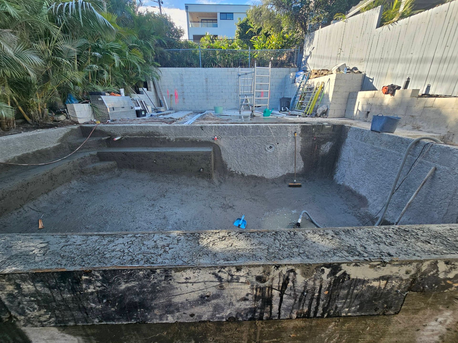 Empty backyard pool under construction with exposed concrete walls and steps.
