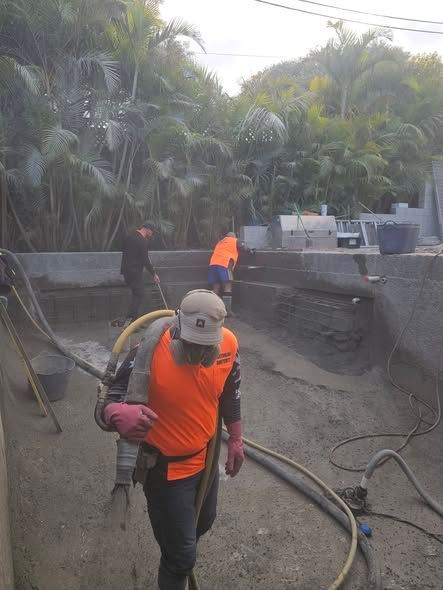 Construction workers in orange safety vests spraying concrete in a trench