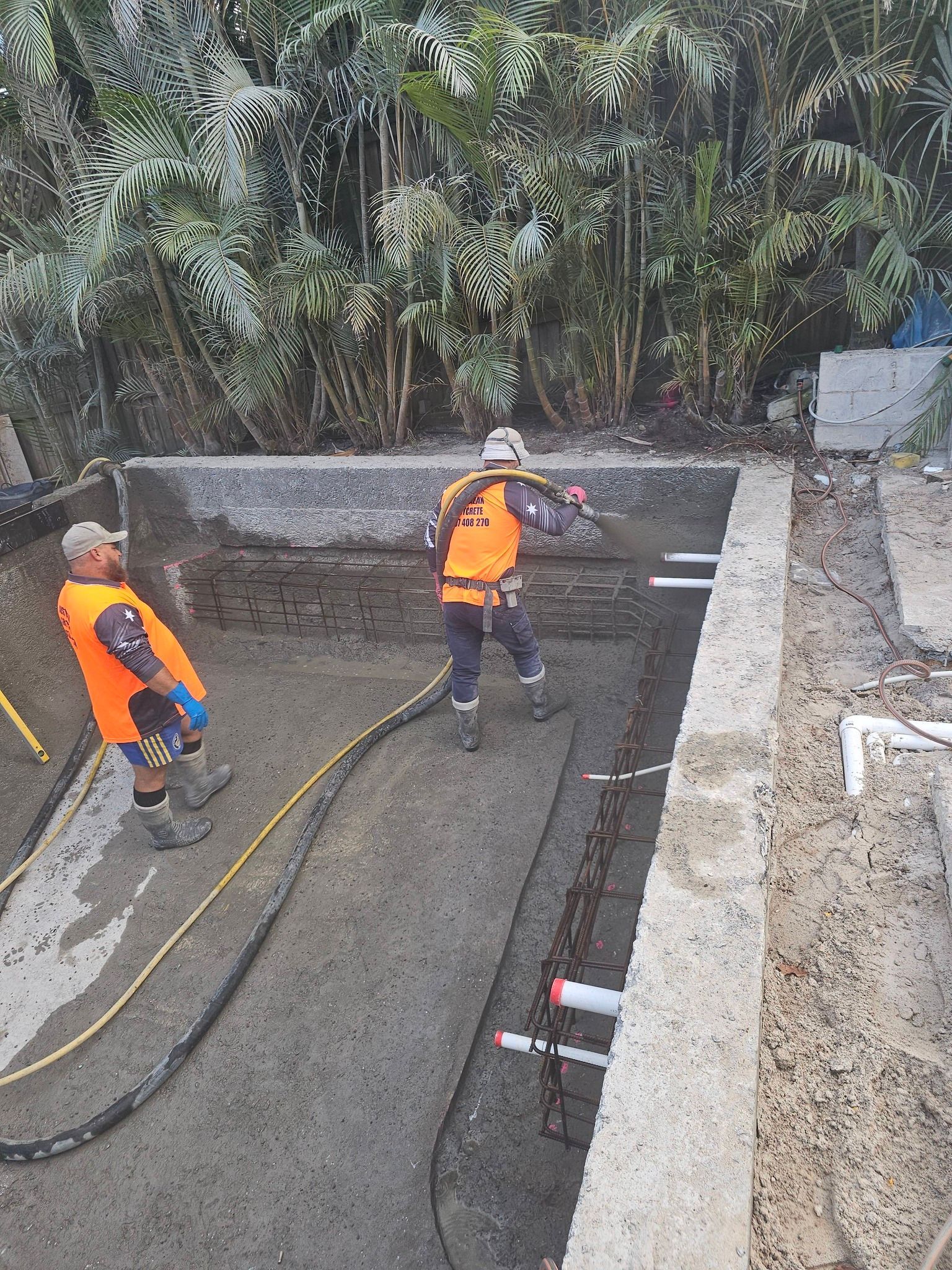 Two workers in orange safety gear using hoses in a construction excavation site