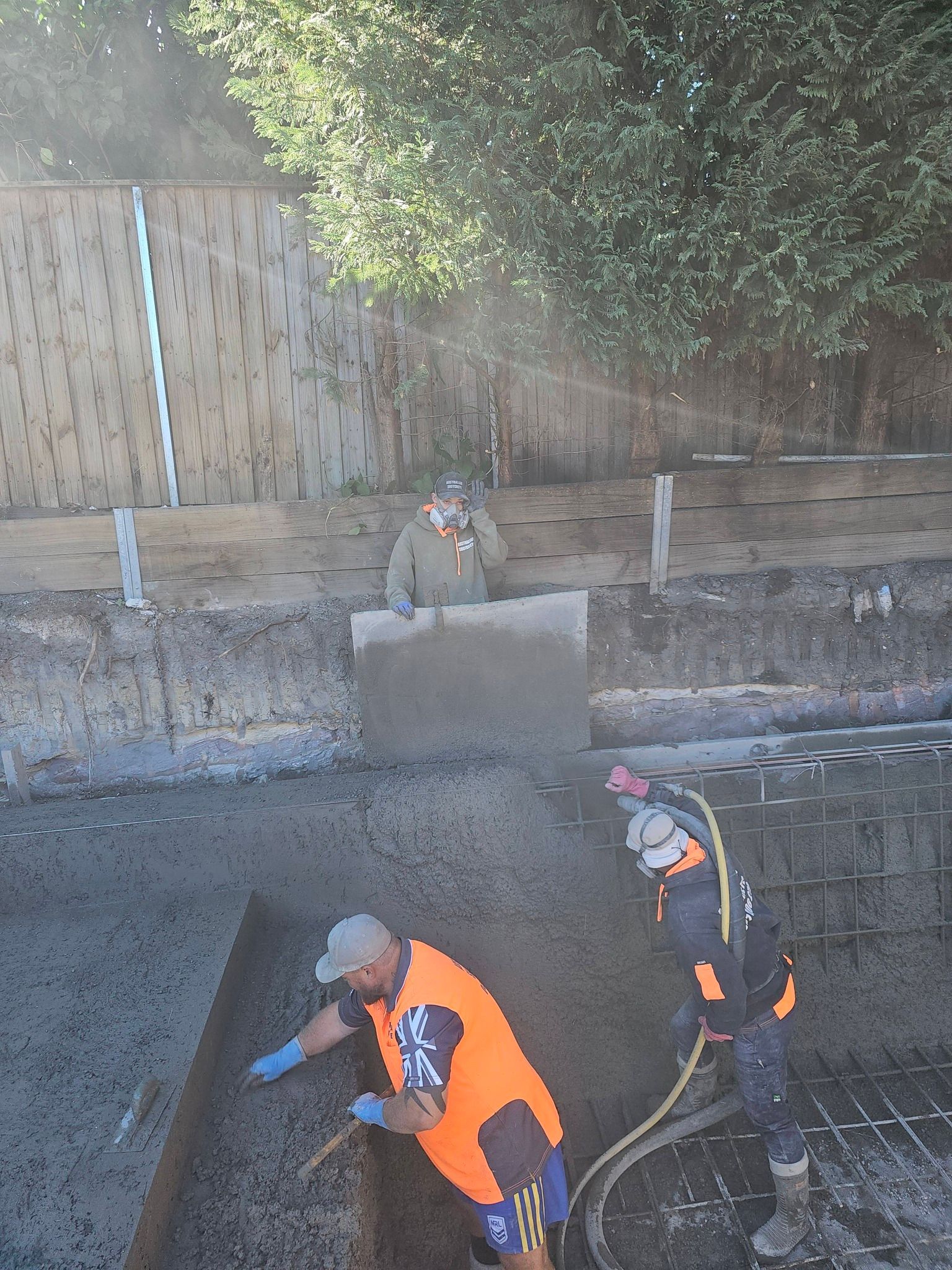 Construction workers in orange vests digging and moving gravel in a trench outdoors