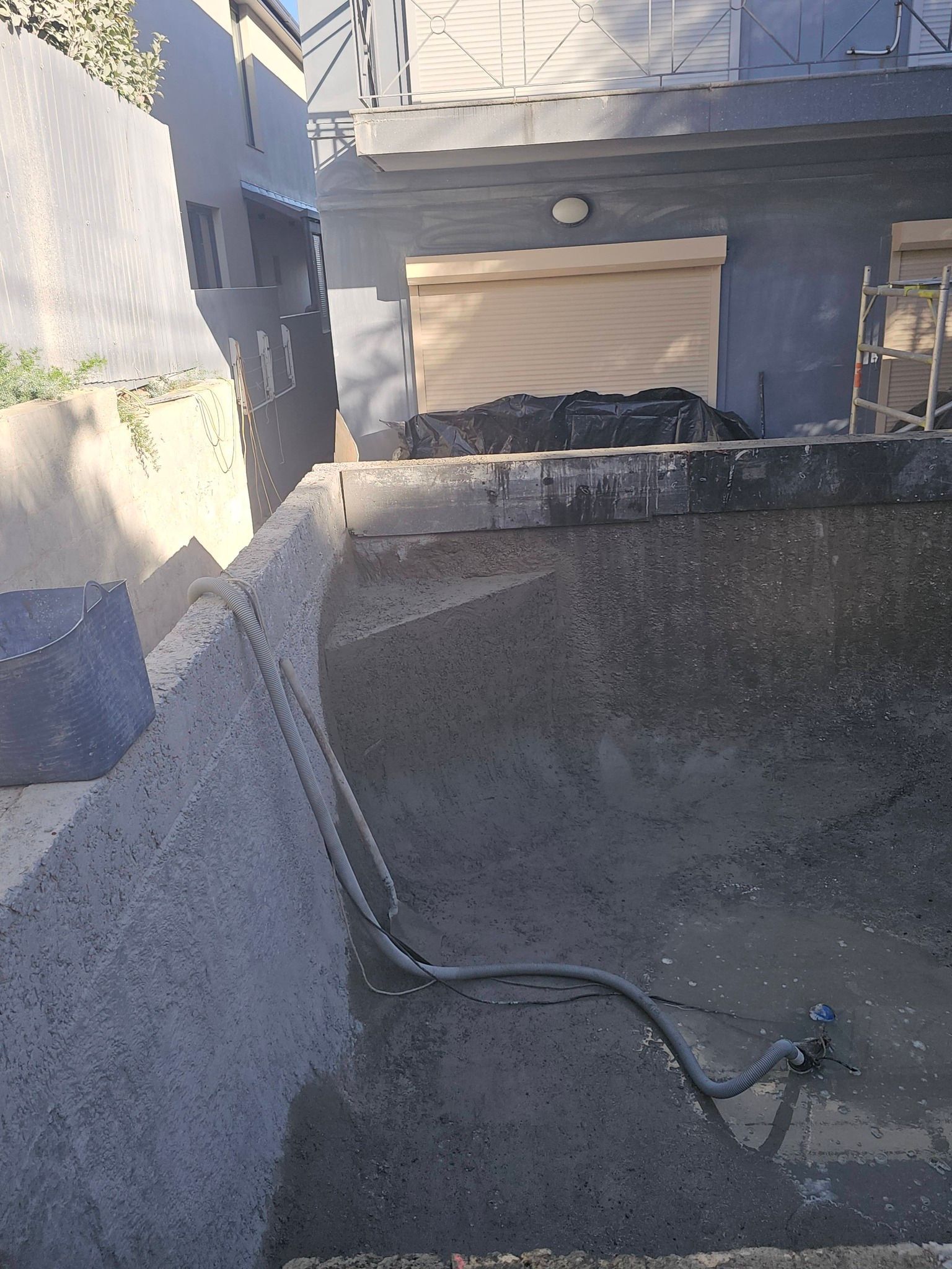 Narrow outdoor concrete alley with a hose on the ground and a blue building wall in sunlight