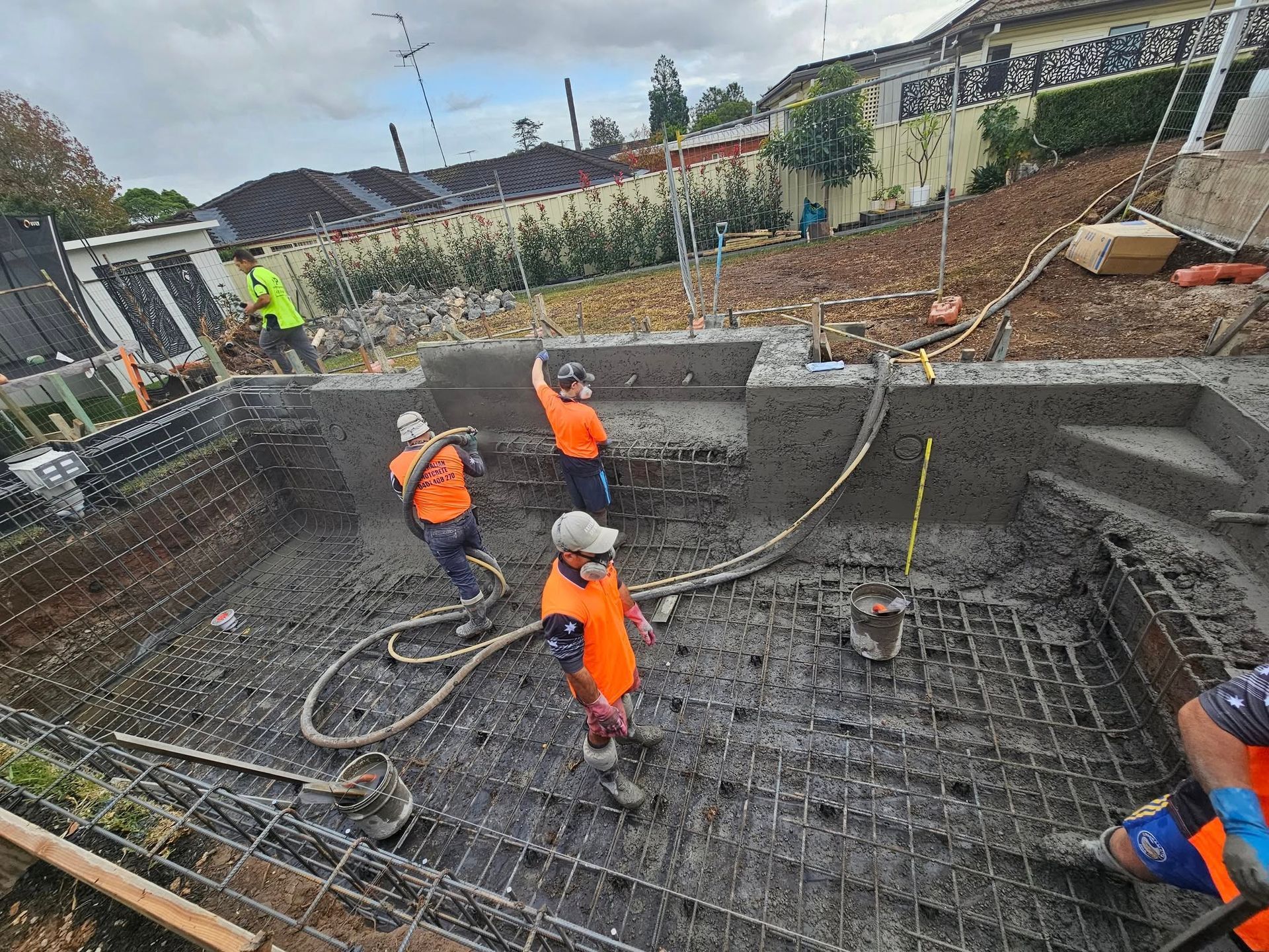 Workers in orange vests applying concrete inside a large circular construction pit
