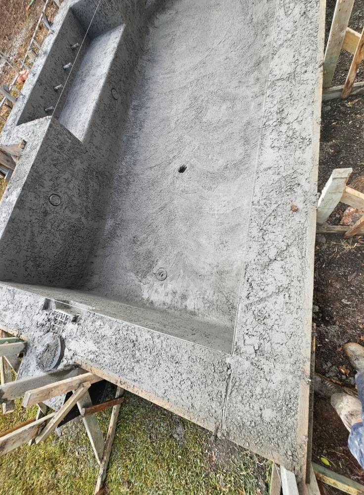 A gray concrete trough or mold lying outdoors amid wood scraps and debris.