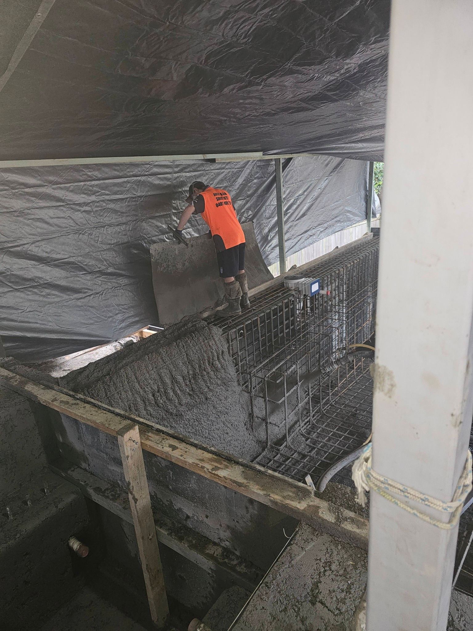 Worker in orange vest on a steep indoor construction or industrial stairwell, spraying or cleaning a dark surface.