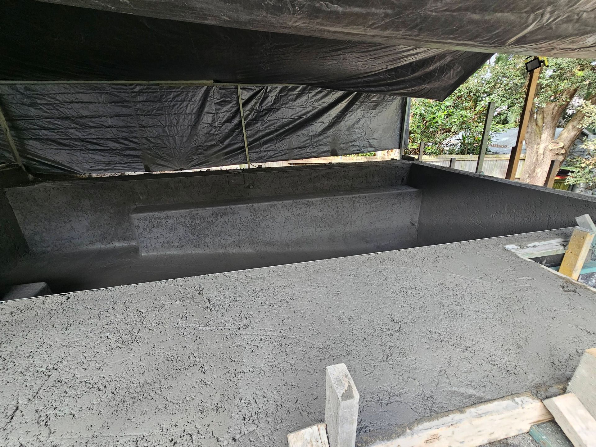 Concrete trough under a black tarp, with a rough concrete ledge in the foreground outdoors.