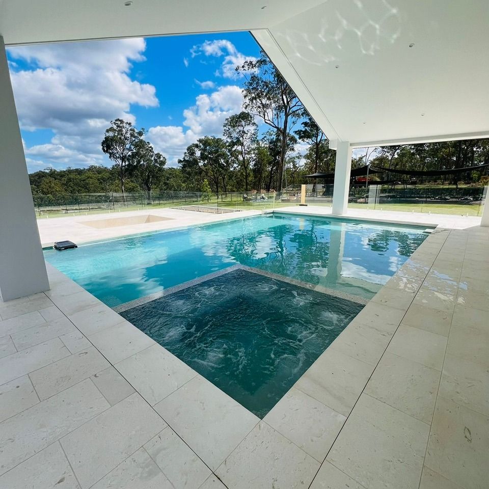 Modern patio with turquoise swimming pool, tiled deck, and sunny tropical yard beyond