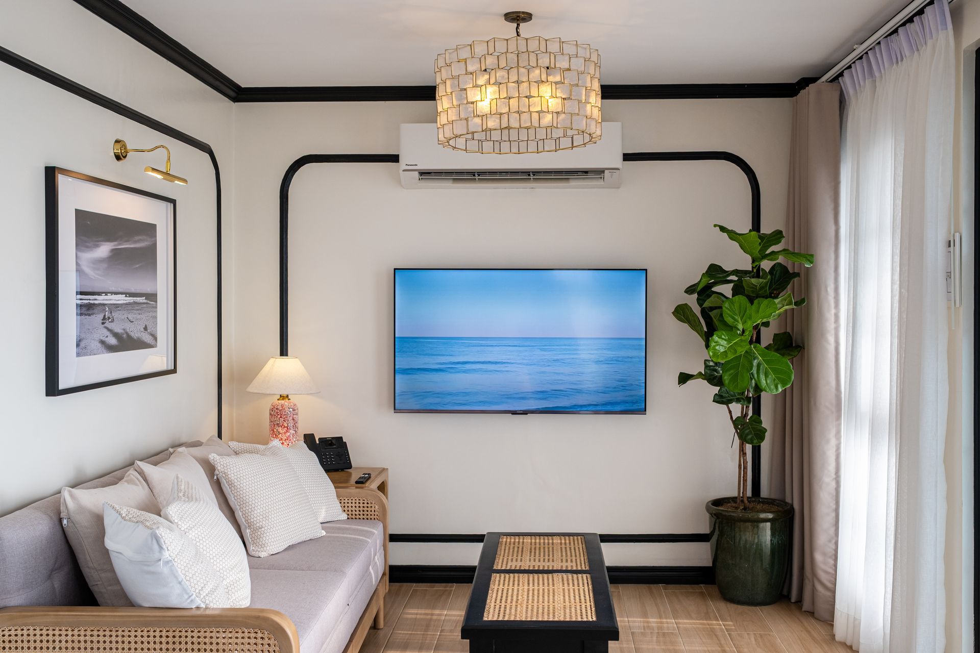 A light-filled living room featuring a sofa with textured pillows, a wall-mounted TV, a potted plant, and black wall trim.