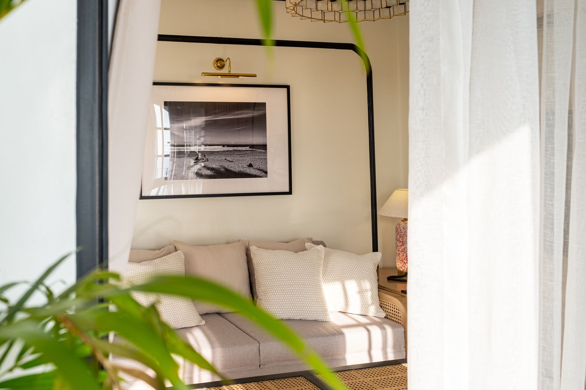 A cozy nook with a sofa, patterned cushions, a framed black-and-white landscape print, and warm lighting.
