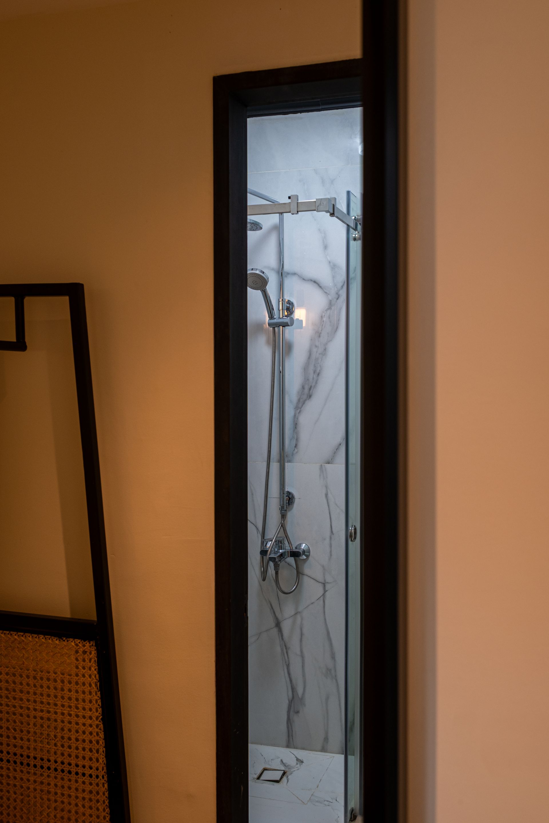A view through a narrow, dark-framed doorway into a shower stall with white marble-patterned tiles and chrome fixtures.