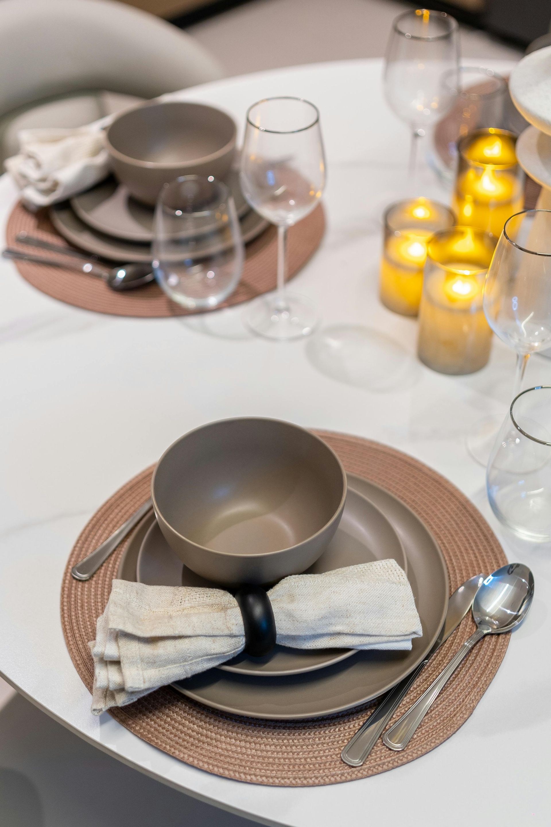 A table setting with two place settings on round placemats, each with a bowl, plates, a napkin, cutlery, and glassware.