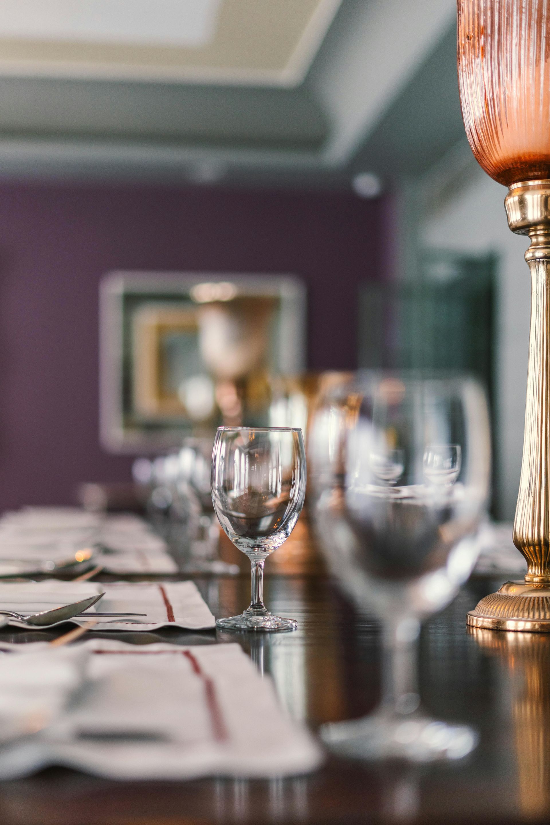 A table is set for dining with clear wine glasses and white placemats, accented by a tall gold candle holder.